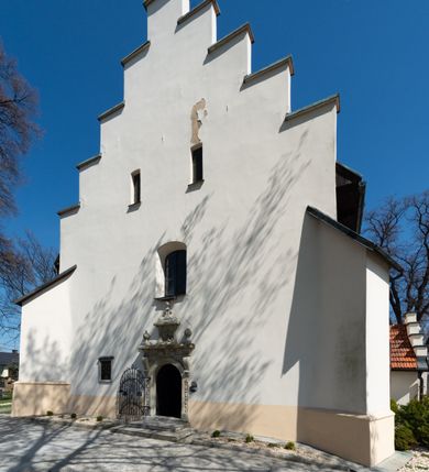 Zdjęcie nr 12: Kościół orientowany, murowany, jednonawowy z węższym prezbiterium zakończonym półkolistą absydą. Przy prezbiterium od północy znajduje się zakrystia, od południa kwadratowa kaplica św. Anny, a przy nawie od południa kruchta. Wnętrze kościoła nakryte jest nowym stropem, natomiast w kaplicy znajduje się sklepienie krzyżowo-żebrowe. Fasada zachodnia ujęta jest na narożnikach skośnymi szkarpami i zwieńczona schodkowym szczytem, podobnie zwieńczona jest kruchta południowa. Portal zachodni kamienny, z belkowaniem wspartym na dwóch liściastych konsolach ponad którymi edikula z płaskorzeźbionym krucyfiksem i klęczącymi postaciami męskimi. Na belkowaniu znajdują się dwa kartusze z herbami: po lewej herb Bończa, a nad nim litery „I” oraz „T”, a na prawo herb Szreniawa i litery „B” i „T”. Portal kruchty południowej jest również kamienny, podobny do zachodniego z inskrypcją: „IN LAVDEM ET GL[ORI]AM DEI O[MN]IP[OTENTIS] HO[NO]RE[M] / B(EATE) M(ARIAE) S(ANCTAE) V(IRGINIS) S(ANCTUS) AEGIDY ET OM(NIUM) SS. FIR. REGNÃTE [TERTIO] SIGISM[UN]DO / REGE POL[ONIAE] Z[?] HEMO[?] EP[ISCOP]O CRAC(OVIENSIS) BERN[AR]DO MACIEIOWSKI / NOVIT[ER] CAR[DINA]LI CRA[COVIENSE] DEI FACTO INTERI[M] PLEBA[N]O R[E]V[EREN]DO SEB(ASTIANO) / NAGRODIO A I SYRADIA PHI[LOSOPHI]AE DOCTORE COLLEG[I]A [MA]IORE / S. T(HEOLOGIAE) PVBLICO PROFES(SORE) PRAEP[OSI]TO S(ANCTA) AN(NAE) CRAC[OVIAE] DECIMARVM / ET FVNDI ECCL(ESIA)E HVIVS P[OST] IVRIS STREPITV(M) RESTITV / TORE ANNO OCTAVO PLEBANAT[U]S SVI. TEMPLVM HO(C) / [ dwa wiersze skute] DE' / NOWO AEDIFICATVM. ET. CONSTRVCTVM. ADIVTORIO / QVORVNDÃ ANNO D[OMINI] MDCIIII MENSE SEPTEMB[RE]”. Od południa świątyni umieszczone są trzy otwory okienne w kształcie stojących prostokątów, zamkniętych łukiem półkolistym, a w prezbiterium dwa małe okrągłe okna. Kościół nakryty jest dwoma dwuspadowymi dachami, nad prezbiterium nieco niższym, nad nawą zwieńczonym wąską i wysoką sygnaturką na dzwon. Wewnątrz świątyni na skrzyżowaniu nawy i prezbiterium umocowana jest drewniana belka tęczowa z ustawionym na niej krucyfiksem i figurami Matki Boskiej i św. Jana Ewangelisty. Chór zachodni drewniany, na planie prostokąta, pośrodku półkoliście zamknięty, wsparty na sześciu filarach, od północnego zachodu z obudowaną boazerią klatką schodową. 