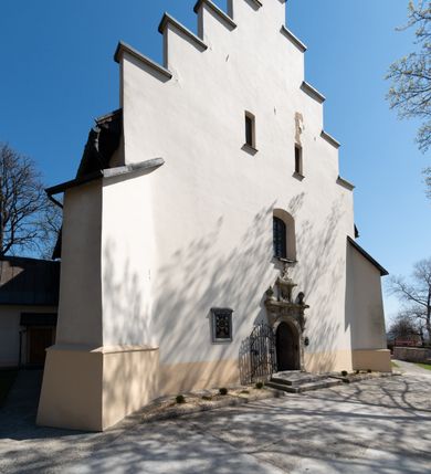 Zdjęcie nr 14: Kościół orientowany, murowany, jednonawowy z węższym prezbiterium zakończonym półkolistą absydą. Przy prezbiterium od północy znajduje się zakrystia, od południa kwadratowa kaplica św. Anny, a przy nawie od południa kruchta. Wnętrze kościoła nakryte jest nowym stropem, natomiast w kaplicy znajduje się sklepienie krzyżowo-żebrowe. Fasada zachodnia ujęta jest na narożnikach skośnymi szkarpami i zwieńczona schodkowym szczytem, podobnie zwieńczona jest kruchta południowa. Portal zachodni kamienny, z belkowaniem wspartym na dwóch liściastych konsolach ponad którymi edikula z płaskorzeźbionym krucyfiksem i klęczącymi postaciami męskimi. Na belkowaniu znajdują się dwa kartusze z herbami: po lewej herb Bończa, a nad nim litery „I” oraz „T”, a na prawo herb Szreniawa i litery „B” i „T”. Portal kruchty południowej jest również kamienny, podobny do zachodniego z inskrypcją: „IN LAVDEM ET GL[ORI]AM DEI O[MN]IP[OTENTIS] HO[NO]RE[M] / B(EATE) M(ARIAE) S(ANCTAE) V(IRGINIS) S(ANCTUS) AEGIDY ET OM(NIUM) SS. FIR. REGNÃTE [TERTIO] SIGISM[UN]DO / REGE POL[ONIAE] Z[?] HEMO[?] EP[ISCOP]O CRAC(OVIENSIS) BERN[AR]DO MACIEIOWSKI / NOVIT[ER] CAR[DINA]LI CRA[COVIENSE] DEI FACTO INTERI[M] PLEBA[N]O R[E]V[EREN]DO SEB(ASTIANO) / NAGRODIO A I SYRADIA PHI[LOSOPHI]AE DOCTORE COLLEG[I]A [MA]IORE / S. T(HEOLOGIAE) PVBLICO PROFES(SORE) PRAEP[OSI]TO S(ANCTA) AN(NAE) CRAC[OVIAE] DECIMARVM / ET FVNDI ECCL(ESIA)E HVIVS P[OST] IVRIS STREPITV(M) RESTITV / TORE ANNO OCTAVO PLEBANAT[U]S SVI. TEMPLVM HO(C) / [ dwa wiersze skute] DE' / NOWO AEDIFICATVM. ET. CONSTRVCTVM. ADIVTORIO / QVORVNDÃ ANNO D[OMINI] MDCIIII MENSE SEPTEMB[RE]”. Od południa świątyni umieszczone są trzy otwory okienne w kształcie stojących prostokątów, zamkniętych łukiem półkolistym, a w prezbiterium dwa małe okrągłe okna. Kościół nakryty jest dwoma dwuspadowymi dachami, nad prezbiterium nieco niższym, nad nawą zwieńczonym wąską i wysoką sygnaturką na dzwon. Wewnątrz świątyni na skrzyżowaniu nawy i prezbiterium umocowana jest drewniana belka tęczowa z ustawionym na niej krucyfiksem i figurami Matki Boskiej i św. Jana Ewangelisty. Chór zachodni drewniany, na planie prostokąta, pośrodku półkoliście zamknięty, wsparty na sześciu filarach, od północnego zachodu z obudowaną boazerią klatką schodową. 