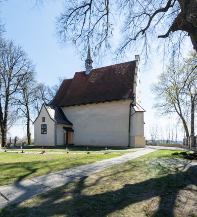 Zdjęcie nr 17: Kościół orientowany, murowany, jednonawowy z węższym prezbiterium zakończonym półkolistą absydą. Przy prezbiterium od północy znajduje się zakrystia, od południa kwadratowa kaplica św. Anny, a przy nawie od południa kruchta. Wnętrze kościoła nakryte jest nowym stropem, natomiast w kaplicy znajduje się sklepienie krzyżowo-żebrowe. Fasada zachodnia ujęta jest na narożnikach skośnymi szkarpami i zwieńczona schodkowym szczytem, podobnie zwieńczona jest kruchta południowa. Portal zachodni kamienny, z belkowaniem wspartym na dwóch liściastych konsolach ponad którymi edikula z płaskorzeźbionym krucyfiksem i klęczącymi postaciami męskimi. Na belkowaniu znajdują się dwa kartusze z herbami: po lewej herb Bończa, a nad nim litery „I” oraz „T”, a na prawo herb Szreniawa i litery „B” i „T”. Portal kruchty południowej jest również kamienny, podobny do zachodniego z inskrypcją: „IN LAVDEM ET GL[ORI]AM DEI O[MN]IP[OTENTIS] HO[NO]RE[M] / B(EATE) M(ARIAE) S(ANCTAE) V(IRGINIS) S(ANCTUS) AEGIDY ET OM(NIUM) SS. FIR. REGNÃTE [TERTIO] SIGISM[UN]DO / REGE POL[ONIAE] Z[?] HEMO[?] EP[ISCOP]O CRAC(OVIENSIS) BERN[AR]DO MACIEIOWSKI / NOVIT[ER] CAR[DINA]LI CRA[COVIENSE] DEI FACTO INTERI[M] PLEBA[N]O R[E]V[EREN]DO SEB(ASTIANO) / NAGRODIO A I SYRADIA PHI[LOSOPHI]AE DOCTORE COLLEG[I]A [MA]IORE / S. T(HEOLOGIAE) PVBLICO PROFES(SORE) PRAEP[OSI]TO S(ANCTA) AN(NAE) CRAC[OVIAE] DECIMARVM / ET FVNDI ECCL(ESIA)E HVIVS P[OST] IVRIS STREPITV(M) RESTITV / TORE ANNO OCTAVO PLEBANAT[U]S SVI. TEMPLVM HO(C) / [ dwa wiersze skute] DE&#039; / NOWO AEDIFICATVM. ET. CONSTRVCTVM. ADIVTORIO / QVORVNDÃ ANNO D[OMINI] MDCIIII MENSE SEPTEMB[RE]”. Od południa świątyni umieszczone są trzy otwory okienne w kształcie stojących prostokątów, zamkniętych łukiem półkolistym, a w prezbiterium dwa małe okrągłe okna. Kościół nakryty jest dwoma dwuspadowymi dachami, nad prezbiterium nieco niższym, nad nawą zwieńczonym wąską i wysoką sygnaturką na dzwon. Wewnątrz świątyni na skrzyżowaniu nawy i prezbiterium umocowana jest drewniana belka tęczowa z ustawionym na niej krucyfiksem i figurami Matki Boskiej i św. Jana Ewangelisty. Chór zachodni drewniany, na planie prostokąta, pośrodku półkoliście zamknięty, wsparty na sześciu filarach, od północnego zachodu z obudowaną boazerią klatką schodową. 