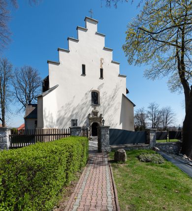 Zdjęcie nr 10: Kościół orientowany, murowany, jednonawowy z węższym prezbiterium zakończonym półkolistą absydą. Przy prezbiterium od północy znajduje się zakrystia, od południa kwadratowa kaplica św. Anny, a przy nawie od południa kruchta. Wnętrze kościoła nakryte jest nowym stropem, natomiast w kaplicy znajduje się sklepienie krzyżowo-żebrowe. Fasada zachodnia ujęta jest na narożnikach skośnymi szkarpami i zwieńczona schodkowym szczytem, podobnie zwieńczona jest kruchta południowa. Portal zachodni kamienny, z belkowaniem wspartym na dwóch liściastych konsolach ponad którymi edikula z płaskorzeźbionym krucyfiksem i klęczącymi postaciami męskimi. Na belkowaniu znajdują się dwa kartusze z herbami: po lewej herb Bończa, a nad nim litery „I” oraz „T”, a na prawo herb Szreniawa i litery „B” i „T”. Portal kruchty południowej jest również kamienny, podobny do zachodniego z inskrypcją: „IN LAVDEM ET GL[ORI]AM DEI O[MN]IP[OTENTIS] HO[NO]RE[M] / B(EATE) M(ARIAE) S(ANCTAE) V(IRGINIS) S(ANCTUS) AEGIDY ET OM(NIUM) SS. FIR. REGNÃTE [TERTIO] SIGISM[UN]DO / REGE POL[ONIAE] Z[?] HEMO[?] EP[ISCOP]O CRAC(OVIENSIS) BERN[AR]DO MACIEIOWSKI / NOVIT[ER] CAR[DINA]LI CRA[COVIENSE] DEI FACTO INTERI[M] PLEBA[N]O R[E]V[EREN]DO SEB(ASTIANO) / NAGRODIO A I SYRADIA PHI[LOSOPHI]AE DOCTORE COLLEG[I]A [MA]IORE / S. T(HEOLOGIAE) PVBLICO PROFES(SORE) PRAEP[OSI]TO S(ANCTA) AN(NAE) CRAC[OVIAE] DECIMARVM / ET FVNDI ECCL(ESIA)E HVIVS P[OST] IVRIS STREPITV(M) RESTITV / TORE ANNO OCTAVO PLEBANAT[U]S SVI. TEMPLVM HO(C) / [ dwa wiersze skute] DE' / NOWO AEDIFICATVM. ET. CONSTRVCTVM. ADIVTORIO / QVORVNDÃ ANNO D[OMINI] MDCIIII MENSE SEPTEMB[RE]”. Od południa świątyni umieszczone są trzy otwory okienne w kształcie stojących prostokątów, zamkniętych łukiem półkolistym, a w prezbiterium dwa małe okrągłe okna. Kościół nakryty jest dwoma dwuspadowymi dachami, nad prezbiterium nieco niższym, nad nawą zwieńczonym wąską i wysoką sygnaturką na dzwon. Wewnątrz świątyni na skrzyżowaniu nawy i prezbiterium umocowana jest drewniana belka tęczowa z ustawionym na niej krucyfiksem i figurami Matki Boskiej i św. Jana Ewangelisty. Chór zachodni drewniany, na planie prostokąta, pośrodku półkoliście zamknięty, wsparty na sześciu filarach, od północnego zachodu z obudowaną boazerią klatką schodową. 