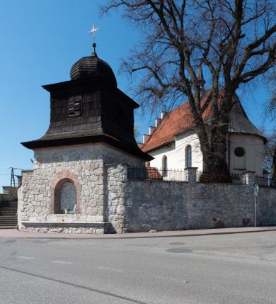Zdjęcie nr 94: Kościół orientowany, murowany, jednonawowy z węższym prezbiterium zakończonym półkolistą absydą. Przy prezbiterium od północy znajduje się zakrystia, od południa kwadratowa kaplica św. Anny, a przy nawie od południa kruchta. Wnętrze kościoła nakryte jest nowym stropem, natomiast w kaplicy znajduje się sklepienie krzyżowo-żebrowe. Fasada zachodnia ujęta jest na narożnikach skośnymi szkarpami i zwieńczona schodkowym szczytem, podobnie zwieńczona jest kruchta południowa. Portal zachodni kamienny, z belkowaniem wspartym na dwóch liściastych konsolach ponad którymi edikula z płaskorzeźbionym krucyfiksem i klęczącymi postaciami męskimi. Na belkowaniu znajdują się dwa kartusze z herbami: po lewej herb Bończa, a nad nim litery „I” oraz „T”, a na prawo herb Szreniawa i litery „B” i „T”. Portal kruchty południowej jest również kamienny, podobny do zachodniego z inskrypcją: „IN LAVDEM ET GL[ORI]AM DEI O[MN]IP[OTENTIS] HO[NO]RE[M] / B(EATE) M(ARIAE) S(ANCTAE) V(IRGINIS) S(ANCTUS) AEGIDY ET OM(NIUM) SS. FIR. REGNÃTE [TERTIO] SIGISM[UN]DO / REGE POL[ONIAE] Z[?] HEMO[?] EP[ISCOP]O CRAC(OVIENSIS) BERN[AR]DO MACIEIOWSKI / NOVIT[ER] CAR[DINA]LI CRA[COVIENSE] DEI FACTO INTERI[M] PLEBA[N]O R[E]V[EREN]DO SEB(ASTIANO) / NAGRODIO A I SYRADIA PHI[LOSOPHI]AE DOCTORE COLLEG[I]A [MA]IORE / S. T(HEOLOGIAE) PVBLICO PROFES(SORE) PRAEP[OSI]TO S(ANCTA) AN(NAE) CRAC[OVIAE] DECIMARVM / ET FVNDI ECCL(ESIA)E HVIVS P[OST] IVRIS STREPITV(M) RESTITV / TORE ANNO OCTAVO PLEBANAT[U]S SVI. TEMPLVM HO(C) / [ dwa wiersze skute] DE' / NOWO AEDIFICATVM. ET. CONSTRVCTVM. ADIVTORIO / QVORVNDÃ ANNO D[OMINI] MDCIIII MENSE SEPTEMB[RE]”. Od południa świątyni umieszczone są trzy otwory okienne w kształcie stojących prostokątów, zamkniętych łukiem półkolistym, a w prezbiterium dwa małe okrągłe okna. Kościół nakryty jest dwoma dwuspadowymi dachami, nad prezbiterium nieco niższym, nad nawą zwieńczonym wąską i wysoką sygnaturką na dzwon. Wewnątrz świątyni na skrzyżowaniu nawy i prezbiterium umocowana jest drewniana belka tęczowa z ustawionym na niej krucyfiksem i figurami Matki Boskiej i św. Jana Ewangelisty. Chór zachodni drewniany, na planie prostokąta, pośrodku półkoliście zamknięty, wsparty na sześciu filarach, od północnego zachodu z obudowaną boazerią klatką schodową. 