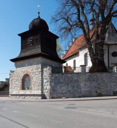 Zdjęcie nr 95: Kościół orientowany, murowany, jednonawowy z węższym prezbiterium zakończonym półkolistą absydą. Przy prezbiterium od północy znajduje się zakrystia, od południa kwadratowa kaplica św. Anny, a przy nawie od południa kruchta. Wnętrze kościoła nakryte jest nowym stropem, natomiast w kaplicy znajduje się sklepienie krzyżowo-żebrowe. Fasada zachodnia ujęta jest na narożnikach skośnymi szkarpami i zwieńczona schodkowym szczytem, podobnie zwieńczona jest kruchta południowa. Portal zachodni kamienny, z belkowaniem wspartym na dwóch liściastych konsolach ponad którymi edikula z płaskorzeźbionym krucyfiksem i klęczącymi postaciami męskimi. Na belkowaniu znajdują się dwa kartusze z herbami: po lewej herb Bończa, a nad nim litery „I” oraz „T”, a na prawo herb Szreniawa i litery „B” i „T”. Portal kruchty południowej jest również kamienny, podobny do zachodniego z inskrypcją: „IN LAVDEM ET GL[ORI]AM DEI O[MN]IP[OTENTIS] HO[NO]RE[M] / B(EATE) M(ARIAE) S(ANCTAE) V(IRGINIS) S(ANCTUS) AEGIDY ET OM(NIUM) SS. FIR. REGNÃTE [TERTIO] SIGISM[UN]DO / REGE POL[ONIAE] Z[?] HEMO[?] EP[ISCOP]O CRAC(OVIENSIS) BERN[AR]DO MACIEIOWSKI / NOVIT[ER] CAR[DINA]LI CRA[COVIENSE] DEI FACTO INTERI[M] PLEBA[N]O R[E]V[EREN]DO SEB(ASTIANO) / NAGRODIO A I SYRADIA PHI[LOSOPHI]AE DOCTORE COLLEG[I]A [MA]IORE / S. T(HEOLOGIAE) PVBLICO PROFES(SORE) PRAEP[OSI]TO S(ANCTA) AN(NAE) CRAC[OVIAE] DECIMARVM / ET FVNDI ECCL(ESIA)E HVIVS P[OST] IVRIS STREPITV(M) RESTITV / TORE ANNO OCTAVO PLEBANAT[U]S SVI. TEMPLVM HO(C) / [ dwa wiersze skute] DE' / NOWO AEDIFICATVM. ET. CONSTRVCTVM. ADIVTORIO / QVORVNDÃ ANNO D[OMINI] MDCIIII MENSE SEPTEMB[RE]”. Od południa świątyni umieszczone są trzy otwory okienne w kształcie stojących prostokątów, zamkniętych łukiem półkolistym, a w prezbiterium dwa małe okrągłe okna. Kościół nakryty jest dwoma dwuspadowymi dachami, nad prezbiterium nieco niższym, nad nawą zwieńczonym wąską i wysoką sygnaturką na dzwon. Wewnątrz świątyni na skrzyżowaniu nawy i prezbiterium umocowana jest drewniana belka tęczowa z ustawionym na niej krucyfiksem i figurami Matki Boskiej i św. Jana Ewangelisty. Chór zachodni drewniany, na planie prostokąta, pośrodku półkoliście zamknięty, wsparty na sześciu filarach, od północnego zachodu z obudowaną boazerią klatką schodową. 