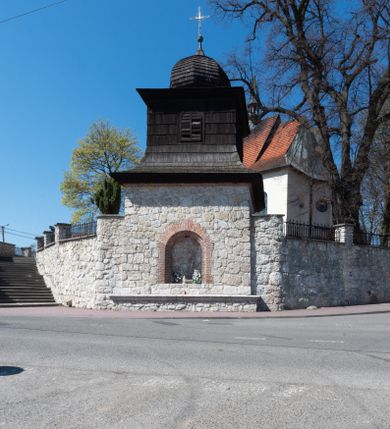 Zdjęcie nr 93: Kościół orientowany, murowany, jednonawowy z węższym prezbiterium zakończonym półkolistą absydą. Przy prezbiterium od północy znajduje się zakrystia, od południa kwadratowa kaplica św. Anny, a przy nawie od południa kruchta. Wnętrze kościoła nakryte jest nowym stropem, natomiast w kaplicy znajduje się sklepienie krzyżowo-żebrowe. Fasada zachodnia ujęta jest na narożnikach skośnymi szkarpami i zwieńczona schodkowym szczytem, podobnie zwieńczona jest kruchta południowa. Portal zachodni kamienny, z belkowaniem wspartym na dwóch liściastych konsolach ponad którymi edikula z płaskorzeźbionym krucyfiksem i klęczącymi postaciami męskimi. Na belkowaniu znajdują się dwa kartusze z herbami: po lewej herb Bończa, a nad nim litery „I” oraz „T”, a na prawo herb Szreniawa i litery „B” i „T”. Portal kruchty południowej jest również kamienny, podobny do zachodniego z inskrypcją: „IN LAVDEM ET GL[ORI]AM DEI O[MN]IP[OTENTIS] HO[NO]RE[M] / B(EATE) M(ARIAE) S(ANCTAE) V(IRGINIS) S(ANCTUS) AEGIDY ET OM(NIUM) SS. FIR. REGNÃTE [TERTIO] SIGISM[UN]DO / REGE POL[ONIAE] Z[?] HEMO[?] EP[ISCOP]O CRAC(OVIENSIS) BERN[AR]DO MACIEIOWSKI / NOVIT[ER] CAR[DINA]LI CRA[COVIENSE] DEI FACTO INTERI[M] PLEBA[N]O R[E]V[EREN]DO SEB(ASTIANO) / NAGRODIO A I SYRADIA PHI[LOSOPHI]AE DOCTORE COLLEG[I]A [MA]IORE / S. T(HEOLOGIAE) PVBLICO PROFES(SORE) PRAEP[OSI]TO S(ANCTA) AN(NAE) CRAC[OVIAE] DECIMARVM / ET FVNDI ECCL(ESIA)E HVIVS P[OST] IVRIS STREPITV(M) RESTITV / TORE ANNO OCTAVO PLEBANAT[U]S SVI. TEMPLVM HO(C) / [ dwa wiersze skute] DE' / NOWO AEDIFICATVM. ET. CONSTRVCTVM. ADIVTORIO / QVORVNDÃ ANNO D[OMINI] MDCIIII MENSE SEPTEMB[RE]”. Od południa świątyni umieszczone są trzy otwory okienne w kształcie stojących prostokątów, zamkniętych łukiem półkolistym, a w prezbiterium dwa małe okrągłe okna. Kościół nakryty jest dwoma dwuspadowymi dachami, nad prezbiterium nieco niższym, nad nawą zwieńczonym wąską i wysoką sygnaturką na dzwon. Wewnątrz świątyni na skrzyżowaniu nawy i prezbiterium umocowana jest drewniana belka tęczowa z ustawionym na niej krucyfiksem i figurami Matki Boskiej i św. Jana Ewangelisty. Chór zachodni drewniany, na planie prostokąta, pośrodku półkoliście zamknięty, wsparty na sześciu filarach, od północnego zachodu z obudowaną boazerią klatką schodową. 