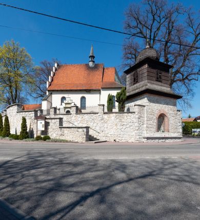 Zdjęcie nr 90: Kościół orientowany, murowany, jednonawowy z węższym prezbiterium zakończonym półkolistą absydą. Przy prezbiterium od północy znajduje się zakrystia, od południa kwadratowa kaplica św. Anny, a przy nawie od południa kruchta. Wnętrze kościoła nakryte jest nowym stropem, natomiast w kaplicy znajduje się sklepienie krzyżowo-żebrowe. Fasada zachodnia ujęta jest na narożnikach skośnymi szkarpami i zwieńczona schodkowym szczytem, podobnie zwieńczona jest kruchta południowa. Portal zachodni kamienny, z belkowaniem wspartym na dwóch liściastych konsolach ponad którymi edikula z płaskorzeźbionym krucyfiksem i klęczącymi postaciami męskimi. Na belkowaniu znajdują się dwa kartusze z herbami: po lewej herb Bończa, a nad nim litery „I” oraz „T”, a na prawo herb Szreniawa i litery „B” i „T”. Portal kruchty południowej jest również kamienny, podobny do zachodniego z inskrypcją: „IN LAVDEM ET GL[ORI]AM DEI O[MN]IP[OTENTIS] HO[NO]RE[M] / B(EATE) M(ARIAE) S(ANCTAE) V(IRGINIS) S(ANCTUS) AEGIDY ET OM(NIUM) SS. FIR. REGNÃTE [TERTIO] SIGISM[UN]DO / REGE POL[ONIAE] Z[?] HEMO[?] EP[ISCOP]O CRAC(OVIENSIS) BERN[AR]DO MACIEIOWSKI / NOVIT[ER] CAR[DINA]LI CRA[COVIENSE] DEI FACTO INTERI[M] PLEBA[N]O R[E]V[EREN]DO SEB(ASTIANO) / NAGRODIO A I SYRADIA PHI[LOSOPHI]AE DOCTORE COLLEG[I]A [MA]IORE / S. T(HEOLOGIAE) PVBLICO PROFES(SORE) PRAEP[OSI]TO S(ANCTA) AN(NAE) CRAC[OVIAE] DECIMARVM / ET FVNDI ECCL(ESIA)E HVIVS P[OST] IVRIS STREPITV(M) RESTITV / TORE ANNO OCTAVO PLEBANAT[U]S SVI. TEMPLVM HO(C) / [ dwa wiersze skute] DE' / NOWO AEDIFICATVM. ET. CONSTRVCTVM. ADIVTORIO / QVORVNDÃ ANNO D[OMINI] MDCIIII MENSE SEPTEMB[RE]”. Od południa świątyni umieszczone są trzy otwory okienne w kształcie stojących prostokątów, zamkniętych łukiem półkolistym, a w prezbiterium dwa małe okrągłe okna. Kościół nakryty jest dwoma dwuspadowymi dachami, nad prezbiterium nieco niższym, nad nawą zwieńczonym wąską i wysoką sygnaturką na dzwon. Wewnątrz świątyni na skrzyżowaniu nawy i prezbiterium umocowana jest drewniana belka tęczowa z ustawionym na niej krucyfiksem i figurami Matki Boskiej i św. Jana Ewangelisty. Chór zachodni drewniany, na planie prostokąta, pośrodku półkoliście zamknięty, wsparty na sześciu filarach, od północnego zachodu z obudowaną boazerią klatką schodową. 