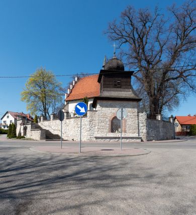 Zdjęcie nr 91: Kościół orientowany, murowany, jednonawowy z węższym prezbiterium zakończonym półkolistą absydą. Przy prezbiterium od północy znajduje się zakrystia, od południa kwadratowa kaplica św. Anny, a przy nawie od południa kruchta. Wnętrze kościoła nakryte jest nowym stropem, natomiast w kaplicy znajduje się sklepienie krzyżowo-żebrowe. Fasada zachodnia ujęta jest na narożnikach skośnymi szkarpami i zwieńczona schodkowym szczytem, podobnie zwieńczona jest kruchta południowa. Portal zachodni kamienny, z belkowaniem wspartym na dwóch liściastych konsolach ponad którymi edikula z płaskorzeźbionym krucyfiksem i klęczącymi postaciami męskimi. Na belkowaniu znajdują się dwa kartusze z herbami: po lewej herb Bończa, a nad nim litery „I” oraz „T”, a na prawo herb Szreniawa i litery „B” i „T”. Portal kruchty południowej jest również kamienny, podobny do zachodniego z inskrypcją: „IN LAVDEM ET GL[ORI]AM DEI O[MN]IP[OTENTIS] HO[NO]RE[M] / B(EATE) M(ARIAE) S(ANCTAE) V(IRGINIS) S(ANCTUS) AEGIDY ET OM(NIUM) SS. FIR. REGNÃTE [TERTIO] SIGISM[UN]DO / REGE POL[ONIAE] Z[?] HEMO[?] EP[ISCOP]O CRAC(OVIENSIS) BERN[AR]DO MACIEIOWSKI / NOVIT[ER] CAR[DINA]LI CRA[COVIENSE] DEI FACTO INTERI[M] PLEBA[N]O R[E]V[EREN]DO SEB(ASTIANO) / NAGRODIO A I SYRADIA PHI[LOSOPHI]AE DOCTORE COLLEG[I]A [MA]IORE / S. T(HEOLOGIAE) PVBLICO PROFES(SORE) PRAEP[OSI]TO S(ANCTA) AN(NAE) CRAC[OVIAE] DECIMARVM / ET FVNDI ECCL(ESIA)E HVIVS P[OST] IVRIS STREPITV(M) RESTITV / TORE ANNO OCTAVO PLEBANAT[U]S SVI. TEMPLVM HO(C) / [ dwa wiersze skute] DE' / NOWO AEDIFICATVM. ET. CONSTRVCTVM. ADIVTORIO / QVORVNDÃ ANNO D[OMINI] MDCIIII MENSE SEPTEMB[RE]”. Od południa świątyni umieszczone są trzy otwory okienne w kształcie stojących prostokątów, zamkniętych łukiem półkolistym, a w prezbiterium dwa małe okrągłe okna. Kościół nakryty jest dwoma dwuspadowymi dachami, nad prezbiterium nieco niższym, nad nawą zwieńczonym wąską i wysoką sygnaturką na dzwon. Wewnątrz świątyni na skrzyżowaniu nawy i prezbiterium umocowana jest drewniana belka tęczowa z ustawionym na niej krucyfiksem i figurami Matki Boskiej i św. Jana Ewangelisty. Chór zachodni drewniany, na planie prostokąta, pośrodku półkoliście zamknięty, wsparty na sześciu filarach, od północnego zachodu z obudowaną boazerią klatką schodową. 