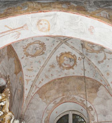 Zdjęcie nr 8: Na ścianie północnej prezbiterium w pierwszej kwaterze od lewej strony została ukazana św. Barbara z mieczem w lewej dłoni i palmą męczeństwa w prawej. W kolejnej kwaterze freski nie zachowały się w całości. W górnej części podwieszone są drapowane tkaniny, po lewej stronie widać dwie uskrzydlone główki aniołków, a po prawej stronie postać nierozpoznanej świętej męczennicy z palmą męczeństwa i księgą w dłoniach. Na ścianie południowej prezbiterium po prawej stronie jest przedstawienie św. Zofii z córkami ujęte w kwaterę w kształcie leżącego prostokąta. Pośrodku znajduje się św. Zofia z rękami złożonymi do modlitwy, na głowie ma zamkniętą koronę, po jej prawie stronie stoją dwie córki, a po lewej trzecia córka. Wszystkie córki zostały ukazane z palmami męczeństwa w dłoniach. Pozostałą powierzchnię ściany wypełniają dekoracje ornamentalne, uskrzydlone anioły, a w dolnej partii zacheuszki. Łuk arkady zdobią arma Christi, które otwierają kolejny cykl przedstawień w kaplicy św. Anny. Prezbiterium obiega od góry szeroki fryz z podwieszoną draperią, pomiędzy którą ukazane są winne grona.