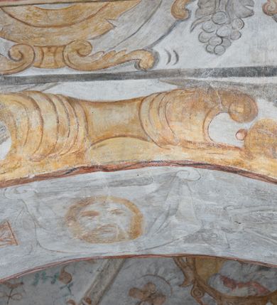 Zdjęcie nr 7: Na ścianie północnej prezbiterium w pierwszej kwaterze od lewej strony została ukazana św. Barbara z mieczem w lewej dłoni i palmą męczeństwa w prawej. W kolejnej kwaterze freski nie zachowały się w całości. W górnej części podwieszone są drapowane tkaniny, po lewej stronie widać dwie uskrzydlone główki aniołków, a po prawej stronie postać nierozpoznanej świętej męczennicy z palmą męczeństwa i księgą w dłoniach. Na ścianie południowej prezbiterium po prawej stronie jest przedstawienie św. Zofii z córkami ujęte w kwaterę w kształcie leżącego prostokąta. Pośrodku znajduje się św. Zofia z rękami złożonymi do modlitwy, na głowie ma zamkniętą koronę, po jej prawie stronie stoją dwie córki, a po lewej trzecia córka. Wszystkie córki zostały ukazane z palmami męczeństwa w dłoniach. Pozostałą powierzchnię ściany wypełniają dekoracje ornamentalne, uskrzydlone anioły, a w dolnej partii zacheuszki. Łuk arkady zdobią arma Christi, które otwierają kolejny cykl przedstawień w kaplicy św. Anny. Prezbiterium obiega od góry szeroki fryz z podwieszoną draperią, pomiędzy którą ukazane są winne grona.