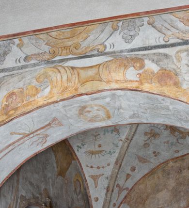 Zdjęcie nr 6: Na ścianie północnej prezbiterium w pierwszej kwaterze od lewej strony została ukazana św. Barbara z mieczem w lewej dłoni i palmą męczeństwa w prawej. W kolejnej kwaterze freski nie zachowały się w całości. W górnej części podwieszone są drapowane tkaniny, po lewej stronie widać dwie uskrzydlone główki aniołków, a po prawej stronie postać nierozpoznanej świętej męczennicy z palmą męczeństwa i księgą w dłoniach. Na ścianie południowej prezbiterium po prawej stronie jest przedstawienie św. Zofii z córkami ujęte w kwaterę w kształcie leżącego prostokąta. Pośrodku znajduje się św. Zofia z rękami złożonymi do modlitwy, na głowie ma zamkniętą koronę, po jej prawie stronie stoją dwie córki, a po lewej trzecia córka. Wszystkie córki zostały ukazane z palmami męczeństwa w dłoniach. Pozostałą powierzchnię ściany wypełniają dekoracje ornamentalne, uskrzydlone anioły, a w dolnej partii zacheuszki. Łuk arkady zdobią arma Christi, które otwierają kolejny cykl przedstawień w kaplicy św. Anny. Prezbiterium obiega od góry szeroki fryz z podwieszoną draperią, pomiędzy którą ukazane są winne grona.