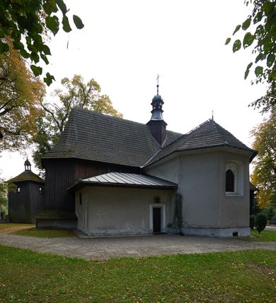 Zdjęcie nr 23: Kościół orientowany, pierwotnie na rzucie krzyża łacińskiego, jednonawowy, z kaplicami bocznymi od północy i południa, z prezbiterium prostokątnym zamkniętym wielobocznie. Obecnie w miejscu drewnianej kaplicy północnej murowana kaplica grobowa, a przy prezbiterium murowana prostokątna zakrystia i skarbczyk (1622 r.); nawa przedłużona ku zachodowi (1878-1879). Przy zachodniej części nawy, od południa, prostokątna drewniana kruchta. Wewnątrz stropy, w kaplicy północnej sklepienie krzyżowe z lunetami, w zakrystii i skarbczyku kolebkowe z lunetami. Zewnątrz zaszalowany. Dach nad nawą i prezbiterium jednokalenicowy, dwuspadowy o załamanych połaciach. Na kalenicy baniasta wieżyczka na sygnaturkę. Odrzwia zachodnie z nadprożem ozdobionym trójliściem z łukiem w ośli grzbiet oraz fryzem arkadkowym; odrzwia z prezbiterium do zakrystii z nadprożem ozdobionym łukiem w ośli grzbiet.