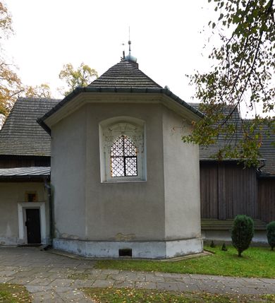 Zdjęcie nr 27: Kościół orientowany, pierwotnie na rzucie krzyża łacińskiego, jednonawowy, z kaplicami bocznymi od północy i południa, z prezbiterium prostokątnym zamkniętym wielobocznie. Obecnie w miejscu drewnianej kaplicy północnej murowana kaplica grobowa, a przy prezbiterium murowana prostokątna zakrystia i skarbczyk (1622 r.); nawa przedłużona ku zachodowi (1878-1879). Przy zachodniej części nawy, od południa, prostokątna drewniana kruchta. Wewnątrz stropy, w kaplicy północnej sklepienie krzyżowe z lunetami, w zakrystii i skarbczyku kolebkowe z lunetami. Zewnątrz zaszalowany. Dach nad nawą i prezbiterium jednokalenicowy, dwuspadowy o załamanych połaciach. Na kalenicy baniasta wieżyczka na sygnaturkę. Odrzwia zachodnie z nadprożem ozdobionym trójliściem z łukiem w ośli grzbiet oraz fryzem arkadkowym; odrzwia z prezbiterium do zakrystii z nadprożem ozdobionym łukiem w ośli grzbiet.