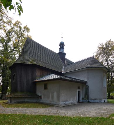 Zdjęcie nr 24: Kościół orientowany, pierwotnie na rzucie krzyża łacińskiego, jednonawowy, z kaplicami bocznymi od północy i południa, z prezbiterium prostokątnym zamkniętym wielobocznie. Obecnie w miejscu drewnianej kaplicy północnej murowana kaplica grobowa, a przy prezbiterium murowana prostokątna zakrystia i skarbczyk (1622 r.); nawa przedłużona ku zachodowi (1878-1879). Przy zachodniej części nawy, od południa, prostokątna drewniana kruchta. Wewnątrz stropy, w kaplicy północnej sklepienie krzyżowe z lunetami, w zakrystii i skarbczyku kolebkowe z lunetami. Zewnątrz zaszalowany. Dach nad nawą i prezbiterium jednokalenicowy, dwuspadowy o załamanych połaciach. Na kalenicy baniasta wieżyczka na sygnaturkę. Odrzwia zachodnie z nadprożem ozdobionym trójliściem z łukiem w ośli grzbiet oraz fryzem arkadkowym; odrzwia z prezbiterium do zakrystii z nadprożem ozdobionym łukiem w ośli grzbiet.