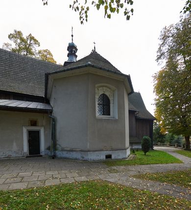 Zdjęcie nr 25: Kościół orientowany, pierwotnie na rzucie krzyża łacińskiego, jednonawowy, z kaplicami bocznymi od północy i południa, z prezbiterium prostokątnym zamkniętym wielobocznie. Obecnie w miejscu drewnianej kaplicy północnej murowana kaplica grobowa, a przy prezbiterium murowana prostokątna zakrystia i skarbczyk (1622 r.); nawa przedłużona ku zachodowi (1878-1879). Przy zachodniej części nawy, od południa, prostokątna drewniana kruchta. Wewnątrz stropy, w kaplicy północnej sklepienie krzyżowe z lunetami, w zakrystii i skarbczyku kolebkowe z lunetami. Zewnątrz zaszalowany. Dach nad nawą i prezbiterium jednokalenicowy, dwuspadowy o załamanych połaciach. Na kalenicy baniasta wieżyczka na sygnaturkę. Odrzwia zachodnie z nadprożem ozdobionym trójliściem z łukiem w ośli grzbiet oraz fryzem arkadkowym; odrzwia z prezbiterium do zakrystii z nadprożem ozdobionym łukiem w ośli grzbiet.