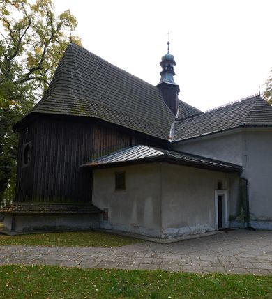 Zdjęcie nr 26: Kościół orientowany, pierwotnie na rzucie krzyża łacińskiego, jednonawowy, z kaplicami bocznymi od północy i południa, z prezbiterium prostokątnym zamkniętym wielobocznie. Obecnie w miejscu drewnianej kaplicy północnej murowana kaplica grobowa, a przy prezbiterium murowana prostokątna zakrystia i skarbczyk (1622 r.); nawa przedłużona ku zachodowi (1878-1879). Przy zachodniej części nawy, od południa, prostokątna drewniana kruchta. Wewnątrz stropy, w kaplicy północnej sklepienie krzyżowe z lunetami, w zakrystii i skarbczyku kolebkowe z lunetami. Zewnątrz zaszalowany. Dach nad nawą i prezbiterium jednokalenicowy, dwuspadowy o załamanych połaciach. Na kalenicy baniasta wieżyczka na sygnaturkę. Odrzwia zachodnie z nadprożem ozdobionym trójliściem z łukiem w ośli grzbiet oraz fryzem arkadkowym; odrzwia z prezbiterium do zakrystii z nadprożem ozdobionym łukiem w ośli grzbiet.