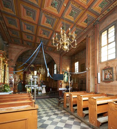 Zdjęcie nr 60: Kościół orientowany, pierwotnie na rzucie krzyża łacińskiego, jednonawowy, z kaplicami bocznymi od północy i południa, z prezbiterium prostokątnym zamkniętym wielobocznie. Obecnie w miejscu drewnianej kaplicy północnej murowana kaplica grobowa, a przy prezbiterium murowana prostokątna zakrystia i skarbczyk (1622 r.); nawa przedłużona ku zachodowi (1878-1879). Przy zachodniej części nawy, od południa, prostokątna drewniana kruchta. Wewnątrz stropy, w kaplicy północnej sklepienie krzyżowe z lunetami, w zakrystii i skarbczyku kolebkowe z lunetami. Zewnątrz zaszalowany. Dach nad nawą i prezbiterium jednokalenicowy, dwuspadowy o załamanych połaciach. Na kalenicy baniasta wieżyczka na sygnaturkę. Odrzwia zachodnie z nadprożem ozdobionym trójliściem z łukiem w ośli grzbiet oraz fryzem arkadkowym; odrzwia z prezbiterium do zakrystii z nadprożem ozdobionym łukiem w ośli grzbiet.