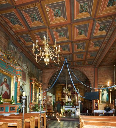 Zdjęcie nr 59: Kościół orientowany, pierwotnie na rzucie krzyża łacińskiego, jednonawowy, z kaplicami bocznymi od północy i południa, z prezbiterium prostokątnym zamkniętym wielobocznie. Obecnie w miejscu drewnianej kaplicy północnej murowana kaplica grobowa, a przy prezbiterium murowana prostokątna zakrystia i skarbczyk (1622 r.); nawa przedłużona ku zachodowi (1878-1879). Przy zachodniej części nawy, od południa, prostokątna drewniana kruchta. Wewnątrz stropy, w kaplicy północnej sklepienie krzyżowe z lunetami, w zakrystii i skarbczyku kolebkowe z lunetami. Zewnątrz zaszalowany. Dach nad nawą i prezbiterium jednokalenicowy, dwuspadowy o załamanych połaciach. Na kalenicy baniasta wieżyczka na sygnaturkę. Odrzwia zachodnie z nadprożem ozdobionym trójliściem z łukiem w ośli grzbiet oraz fryzem arkadkowym; odrzwia z prezbiterium do zakrystii z nadprożem ozdobionym łukiem w ośli grzbiet.