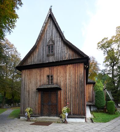 Zdjęcie nr 10: Kościół orientowany, pierwotnie na rzucie krzyża łacińskiego, jednonawowy, z kaplicami bocznymi od północy i południa, z prezbiterium prostokątnym zamkniętym wielobocznie. Obecnie w miejscu drewnianej kaplicy północnej murowana kaplica grobowa, a przy prezbiterium murowana prostokątna zakrystia i skarbczyk (1622 r.); nawa przedłużona ku zachodowi (1878-1879). Przy zachodniej części nawy, od południa, prostokątna drewniana kruchta. Wewnątrz stropy, w kaplicy północnej sklepienie krzyżowe z lunetami, w zakrystii i skarbczyku kolebkowe z lunetami. Zewnątrz zaszalowany. Dach nad nawą i prezbiterium jednokalenicowy, dwuspadowy o załamanych połaciach. Na kalenicy baniasta wieżyczka na sygnaturkę. Odrzwia zachodnie z nadprożem ozdobionym trójliściem z łukiem w ośli grzbiet oraz fryzem arkadkowym; odrzwia z prezbiterium do zakrystii z nadprożem ozdobionym łukiem w ośli grzbiet.