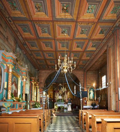 Zdjęcie nr 58: Kościół orientowany, pierwotnie na rzucie krzyża łacińskiego, jednonawowy, z kaplicami bocznymi od północy i południa, z prezbiterium prostokątnym zamkniętym wielobocznie. Obecnie w miejscu drewnianej kaplicy północnej murowana kaplica grobowa, a przy prezbiterium murowana prostokątna zakrystia i skarbczyk (1622 r.); nawa przedłużona ku zachodowi (1878-1879). Przy zachodniej części nawy, od południa, prostokątna drewniana kruchta. Wewnątrz stropy, w kaplicy północnej sklepienie krzyżowe z lunetami, w zakrystii i skarbczyku kolebkowe z lunetami. Zewnątrz zaszalowany. Dach nad nawą i prezbiterium jednokalenicowy, dwuspadowy o załamanych połaciach. Na kalenicy baniasta wieżyczka na sygnaturkę. Odrzwia zachodnie z nadprożem ozdobionym trójliściem z łukiem w ośli grzbiet oraz fryzem arkadkowym; odrzwia z prezbiterium do zakrystii z nadprożem ozdobionym łukiem w ośli grzbiet.