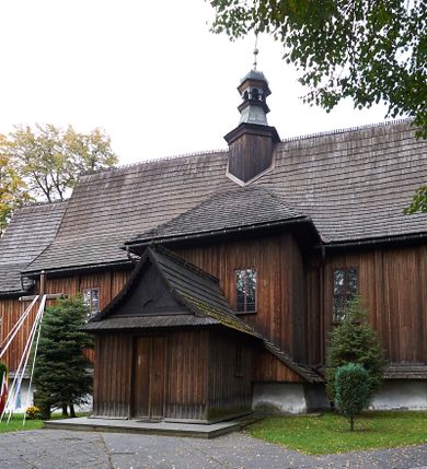 Zdjęcie nr 12: Kościół orientowany, pierwotnie na rzucie krzyża łacińskiego, jednonawowy, z kaplicami bocznymi od północy i południa, z prezbiterium prostokątnym zamkniętym wielobocznie. Obecnie w miejscu drewnianej kaplicy północnej murowana kaplica grobowa, a przy prezbiterium murowana prostokątna zakrystia i skarbczyk (1622 r.); nawa przedłużona ku zachodowi (1878-1879). Przy zachodniej części nawy, od południa, prostokątna drewniana kruchta. Wewnątrz stropy, w kaplicy północnej sklepienie krzyżowe z lunetami, w zakrystii i skarbczyku kolebkowe z lunetami. Zewnątrz zaszalowany. Dach nad nawą i prezbiterium jednokalenicowy, dwuspadowy o załamanych połaciach. Na kalenicy baniasta wieżyczka na sygnaturkę. Odrzwia zachodnie z nadprożem ozdobionym trójliściem z łukiem w ośli grzbiet oraz fryzem arkadkowym; odrzwia z prezbiterium do zakrystii z nadprożem ozdobionym łukiem w ośli grzbiet.