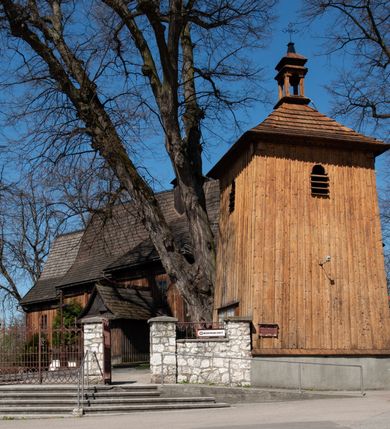 Zdjęcie nr 5: Kościół orientowany, pierwotnie na rzucie krzyża łacińskiego, jednonawowy, z kaplicami bocznymi od północy i południa, z prezbiterium prostokątnym zamkniętym wielobocznie. Obecnie w miejscu drewnianej kaplicy północnej murowana kaplica grobowa, a przy prezbiterium murowana prostokątna zakrystia i skarbczyk (1622 r.); nawa przedłużona ku zachodowi (1878-1879). Przy zachodniej części nawy, od południa, prostokątna drewniana kruchta. Wewnątrz stropy, w kaplicy północnej sklepienie krzyżowe z lunetami, w zakrystii i skarbczyku kolebkowe z lunetami. Zewnątrz zaszalowany. Dach nad nawą i prezbiterium jednokalenicowy, dwuspadowy o załamanych połaciach. Na kalenicy baniasta wieżyczka na sygnaturkę. Odrzwia zachodnie z nadprożem ozdobionym trójliściem z łukiem w ośli grzbiet oraz fryzem arkadkowym; odrzwia z prezbiterium do zakrystii z nadprożem ozdobionym łukiem w ośli grzbiet.