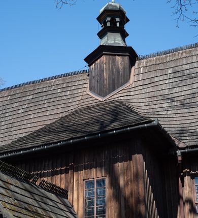 Zdjęcie nr 17: Kościół orientowany, pierwotnie na rzucie krzyża łacińskiego, jednonawowy, z kaplicami bocznymi od północy i południa, z prezbiterium prostokątnym zamkniętym wielobocznie. Obecnie w miejscu drewnianej kaplicy północnej murowana kaplica grobowa, a przy prezbiterium murowana prostokątna zakrystia i skarbczyk (1622 r.); nawa przedłużona ku zachodowi (1878-1879). Przy zachodniej części nawy, od południa, prostokątna drewniana kruchta. Wewnątrz stropy, w kaplicy północnej sklepienie krzyżowe z lunetami, w zakrystii i skarbczyku kolebkowe z lunetami. Zewnątrz zaszalowany. Dach nad nawą i prezbiterium jednokalenicowy, dwuspadowy o załamanych połaciach. Na kalenicy baniasta wieżyczka na sygnaturkę. Odrzwia zachodnie z nadprożem ozdobionym trójliściem z łukiem w ośli grzbiet oraz fryzem arkadkowym; odrzwia z prezbiterium do zakrystii z nadprożem ozdobionym łukiem w ośli grzbiet.