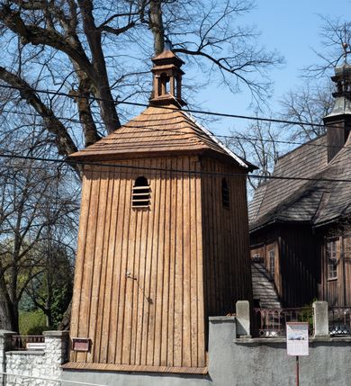 Zdjęcie nr 6: Kościół orientowany, pierwotnie na rzucie krzyża łacińskiego, jednonawowy, z kaplicami bocznymi od północy i południa, z prezbiterium prostokątnym zamkniętym wielobocznie. Obecnie w miejscu drewnianej kaplicy północnej murowana kaplica grobowa, a przy prezbiterium murowana prostokątna zakrystia i skarbczyk (1622 r.); nawa przedłużona ku zachodowi (1878-1879). Przy zachodniej części nawy, od południa, prostokątna drewniana kruchta. Wewnątrz stropy, w kaplicy północnej sklepienie krzyżowe z lunetami, w zakrystii i skarbczyku kolebkowe z lunetami. Zewnątrz zaszalowany. Dach nad nawą i prezbiterium jednokalenicowy, dwuspadowy o załamanych połaciach. Na kalenicy baniasta wieżyczka na sygnaturkę. Odrzwia zachodnie z nadprożem ozdobionym trójliściem z łukiem w ośli grzbiet oraz fryzem arkadkowym; odrzwia z prezbiterium do zakrystii z nadprożem ozdobionym łukiem w ośli grzbiet.