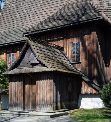 Zdjęcie nr 13: Kościół orientowany, pierwotnie na rzucie krzyża łacińskiego, jednonawowy, z kaplicami bocznymi od północy i południa, z prezbiterium prostokątnym zamkniętym wielobocznie. Obecnie w miejscu drewnianej kaplicy północnej murowana kaplica grobowa, a przy prezbiterium murowana prostokątna zakrystia i skarbczyk (1622 r.); nawa przedłużona ku zachodowi (1878-1879). Przy zachodniej części nawy, od południa, prostokątna drewniana kruchta. Wewnątrz stropy, w kaplicy północnej sklepienie krzyżowe z lunetami, w zakrystii i skarbczyku kolebkowe z lunetami. Zewnątrz zaszalowany. Dach nad nawą i prezbiterium jednokalenicowy, dwuspadowy o załamanych połaciach. Na kalenicy baniasta wieżyczka na sygnaturkę. Odrzwia zachodnie z nadprożem ozdobionym trójliściem z łukiem w ośli grzbiet oraz fryzem arkadkowym; odrzwia z prezbiterium do zakrystii z nadprożem ozdobionym łukiem w ośli grzbiet.