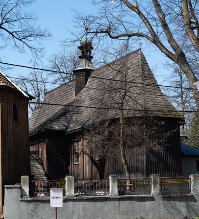 Zdjęcie nr 20: Kościół orientowany, pierwotnie na rzucie krzyża łacińskiego, jednonawowy, z kaplicami bocznymi od północy i południa, z prezbiterium prostokątnym zamkniętym wielobocznie. Obecnie w miejscu drewnianej kaplicy północnej murowana kaplica grobowa, a przy prezbiterium murowana prostokątna zakrystia i skarbczyk (1622 r.); nawa przedłużona ku zachodowi (1878-1879). Przy zachodniej części nawy, od południa, prostokątna drewniana kruchta. Wewnątrz stropy, w kaplicy północnej sklepienie krzyżowe z lunetami, w zakrystii i skarbczyku kolebkowe z lunetami. Zewnątrz zaszalowany. Dach nad nawą i prezbiterium jednokalenicowy, dwuspadowy o załamanych połaciach. Na kalenicy baniasta wieżyczka na sygnaturkę. Odrzwia zachodnie z nadprożem ozdobionym trójliściem z łukiem w ośli grzbiet oraz fryzem arkadkowym; odrzwia z prezbiterium do zakrystii z nadprożem ozdobionym łukiem w ośli grzbiet.