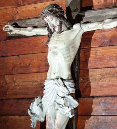 Zdjęcie nr 1: Chrystus rozpięty na krzyżu z głową opuszczoną na pierś, z wyprostowanymi poziomo rękami i wyprostowanymi nogami, ze stopami założonymi prawa na lewą i przybitymi jednym gwoździem. Ciało wychudzone, z podkreśloną budową anatomiczną i naprężoną muskulaturą, z rozdętą klatką piersiową i wklęsłym brzuchem. Twarz pociągła, z długim nosem i zapadniętymi policzkami, okolona krótką brodą i włosami opadającymi na barki, z pasmem włosów spływającym na prawy obojczyk. Na włosy nałożona korona cierniowa upleciona z dwóch cienkich gałązek. Wokół bioder perizonium przewiązane z przodu, po lewej stronie brzucha, z dwoma dekoracyjnie udrapowanymi i rozwianymi końcami. Na górnej belce krzyża ułożony poziomo titulus o kształcie lekko pofałdowanej wstęgi z końcami wyciętymi w jaskółczy ogon, z literami : J. N. R. J. Karnacja ciała w jasnym odcieniu, włosy i broda brązowe, perizonium i titulus białe, krzyż w kolorze naturalnego drewna.