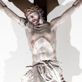 Zdjęcie nr 1: Chrystus rozpięty na krzyżu w silnym zwisie ciała, z szeroko rozłożonymi rękami, z głową opuszczoną na prawy bark, z nogami ugiętymi w kolanach; stopy założone lewa na prawą i przybite jednym gwoździem. Ciało esowato wygięte, muskularne, z podkreśloną budową anatomiczną. W prawym boku rana. Twarz trójkątna, z wydatnym nosem i kośćmi policzkowymi, okolona krótką brodą i włosami spływającymi na plecy, odsłaniającymi szyję i lewy bark, z kosmykiem włosów na prawym barku. Na włosy nałożona korona cierniowa upleciona z trzech grubych gałązek. Wokół bioder sznur podtrzymujący perizonium, które nie osłania prawego biodra, z końcem zwisającym wzdłuż prawego uda. Na górnej belce krzyża ułożony pionowo titulus o kształcie lekko pofałdowanej wstęgi z końcem wyciętym w jaskółczy ogon, z literami : J. N. / R. J. Karnacja ciała w jasnym odcieniu, z czerwonymi plamami krwi, włosy i broda brązowe, perizonium i titulus białe, krzyż w kolorze naturalnego drewna.