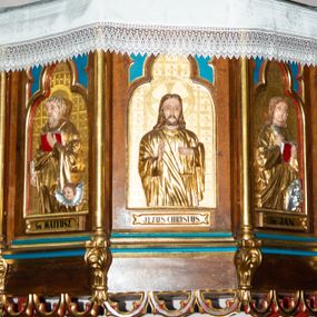 Zdjęcie nr 1: Ambona przyścienna, wisząca, z wejściem od strony zakrystii. Kosz na planie ośmioboku; ścianki wydzielone wąskimi kolumienkami, stojącymi na wspornikach; w polach płyciny w formie stojącego prostokąta, zamkniętego łukiem trójlistnym z maswerkami w przyłuczach, wewnątrz płaskorzeźbione półpostacie: św. Łukasza, św. Mateusza, Jezusa Chrystusa, św. Jana i św. Marka. Ewangeliści ukazani są frontalnie w trzech czwartych, z księgami oraz z piórami do pisania w dłoniach. Jezus z dłońmi ułożonymi w geście błogosławieństwa. Ubrani są w złote suknie i płaszcze. Wokół głów mają złote i koliste nimby; Jezus nimb krzyżowy. Ewangelistom towarzyszą ich symbole: św. Łukaszowi – byk, św. Mateuszowi – uskrzydlona główka aniołka, św. Janowi – orzeł, a św. Markowi – lew. Pod każdą płyciną znajdują się banderole z podpisami, kolejno od lewej: „Św(ięty) ŁUKASZ”, „Św(ięty) MATEUSZ”, „JEZUS CHRYSTUS”, „Św(ięty) JAN”, „Św(ięty) MAREK”. Tła płycin zapełnia kratownica, której kwadratowe pola wypełniają greckie krzyżyki. Dolna krawędź kosza zdobiona jest neogotyckim fartuchem; parapet ma formę gzymsu. 

Zaplecek wąski, ujęty parą kolumienek; w polu drzwi o kształcie prostokąta stojącego dekorowane dwiema płycinami z maswerkami; nad nimi prostokątna płaskorzeźba z przedstawieniem płynącej łodzi z monogramem Chrystusa na tle rozpiętego żagla. 

Baldachim powtarzający plan kosza, w formie podstawy dla ośmiobocznej ażurowej wieżyczki z blendami w ściankach i łukami przyporowymi, dekorowanej żabkami. Krawędź baldachimu profilowana, dekorowana sterczynami w narożach i neogotyckimi fartuchami u spodu i u góry. W podniebiu rzeźbiona gołębica Ducha Świętego w glorii.  

Struktura w kolorze naturalnego drewna; płyciny polichromowane na niebiesko i czerwono; elementy architektoniczne, profile, kolumienki i ścianki kosza złocone.
