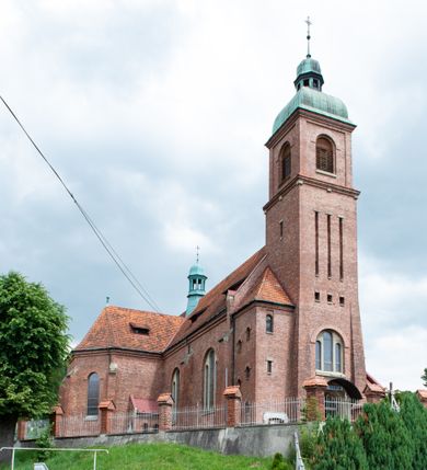 Zdjęcie nr 2: Kościół na planie krzyża łacińskiego, jednonawowy, z transeptem, zamknięty trójbocznym prezbiterium od północy i dobudowaną do niego zakrystią; na skrzyżowaniu nawy głównej i ramion transeptu wieżyczka na sygnaturkę. Fasadę tworzy masywna wieża, zwieńczona hełmem pokrytym blachą miedzianą. Główne wejście do kościoła od strony południowej, poprzez neoromański portal; wejścia boczne zlokalizowane od wschodu i zachodu, na styku nawy głównej i transeptu poprzez niewielkie kruchty. W oknach, w nawie współczesne witraże przedstawiające tajemnice różańca świętego; w prezbiterium Chrystusa ukrzyżowanego, św. Jana Pawła II i kardynała Stefana Wyszyńskiego, a w transepcie świętych zakonników: M. M. Alacoque, brata Alberta i siostrę Faustynę oraz św. Maksymiliana Marię Kolbego i bł. księdza Jerzego Popiełuszkę.
