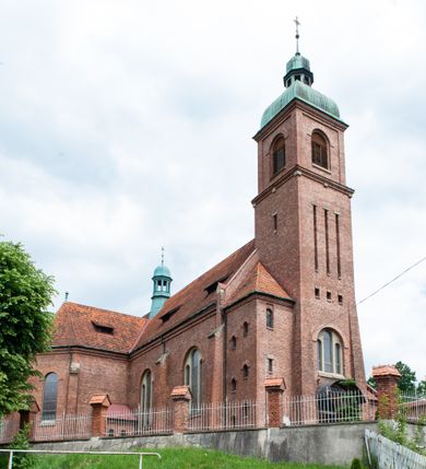 Zdjęcie nr 13: Kościół na planie krzyża łacińskiego, jednonawowy, z transeptem, zamknięty trójbocznym prezbiterium od północy i dobudowaną do niego zakrystią; na skrzyżowaniu nawy głównej i ramion transeptu wieżyczka na sygnaturkę. Fasadę tworzy masywna wieża, zwieńczona hełmem pokrytym blachą miedzianą. Główne wejście do kościoła od strony południowej, poprzez neoromański portal; wejścia boczne zlokalizowane od wschodu i zachodu, na styku nawy głównej i transeptu poprzez niewielkie kruchty. W oknach, w nawie współczesne witraże przedstawiające tajemnice różańca świętego; w prezbiterium Chrystusa ukrzyżowanego, św. Jana Pawła II i kardynała Stefana Wyszyńskiego, a w transepcie świętych zakonników: M. M. Alacoque, brata Alberta i siostrę Faustynę oraz św. Maksymiliana Marię Kolbego i bł. księdza Jerzego Popiełuszkę.
