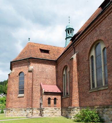 Zdjęcie nr 23: Kościół na planie krzyża łacińskiego, jednonawowy, z transeptem, zamknięty trójbocznym prezbiterium od północy i dobudowaną do niego zakrystią; na skrzyżowaniu nawy głównej i ramion transeptu wieżyczka na sygnaturkę. Fasadę tworzy masywna wieża, zwieńczona hełmem pokrytym blachą miedzianą. Główne wejście do kościoła od strony południowej, poprzez neoromański portal; wejścia boczne zlokalizowane od wschodu i zachodu, na styku nawy głównej i transeptu poprzez niewielkie kruchty. W oknach, w nawie współczesne witraże przedstawiające tajemnice różańca świętego; w prezbiterium Chrystusa ukrzyżowanego, św. Jana Pawła II i kardynała Stefana Wyszyńskiego, a w transepcie świętych zakonników: M. M. Alacoque, brata Alberta i siostrę Faustynę oraz św. Maksymiliana Marię Kolbego i bł. księdza Jerzego Popiełuszkę.
