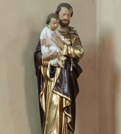 Zdjęcie nr 1: Rzeźba ustawiona na wysokim, profilowanym, prostopadłościennym cokole, w górnej części o ściętych narożach. Święty Józef został ukazany w postawie stojącej, w delikatnym kontrapoście, z prawą nogą ugiętą w kolanie, z Dzieciątkiem Jezus na prawym ręku, lewą ręką święty przyciska do piersi białą lilię, a dłonią podtrzymuje siedzącego Jezusa. Święty Józef ubrany w złotą, długą suknię z długimi rękawami oraz brązowy płaszcz. Jego twarz jest podłużna, o podkreślonych kościach policzkowych, z długim i wąskim nosem, małymi i drobnymi ustami, okolona średniej długości brodą, rozdzieloną na dwa pukle oraz średniej długości, ciemnobrązowymi włosami. Dzieciątko Jezus zwrócone trzy czwarte w lewo, w pozycji siedzącej, z rękami rozpostartymi szeroko na boki. Ubrane w długą, białą sukienkę, obwiedzioną na brzegach złotą lamówką. Twarz okrągła, z długim i szerokim nosem, z zarumienionymi policzkami; włosy jasnobrązowe, kędzierzawe, z wyraźnymi zakolami. Polichromia w odsłoniętych partiach ciała naturalistyczna. 
