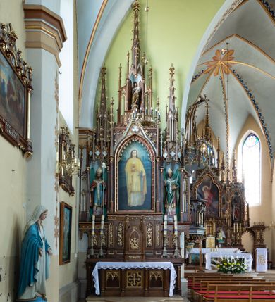 Zdjęcie nr 1: Neogotycki, przyścienny, jednokondygnacyjny ołtarz Matki Boskiej Różańcowej uzyskał architektoniczną strukturę ze zwieńczeniem. Kolorystyka ołtarza utrzymana została w tonacji ciemnego, bejcowanego drewna. Detale, ornamenty zostały wyzłocone, natomiast wypełnienia maswerków i ram wimperg są białe. Z kolei pole ramy głównego obrazu wykonano jako czerwone. Retabulum ustawiono na podwójnych gradusach zaokrąglonych od przodu. Stipes ołtarzowy uzyskał kształt prostopadłościanu z trzema czworobocznymi płycinami od frontu, ujętymi złoconymi i profilowanymi obramieniami. Płyciny rozdzielają  półkolumienki na wysokich cokolikach. Dwie skrajne płyciny stipesu wypełniono u góry maswerkiem, natomiast w środkowej znalazł się równoramienny krzyż wpisany w czteroliść. Stipes podtrzymuje drewnianą mensę z portatylem. Ołtarz przylega do wysokiego, prostopadłościennego cokołu flankowanego po bokach kolumienkami, na którym wspiera się cała nastawa. Widoczne jego partie zdobią prostokątne płyciny w obramieniach. Na cokole wspiera się predella podzielona płytkimi, prostokątnymi płycinami zakończonymi ostrołukowymi arkadkami z noskami, wypełnionymi płaskorzeźbionym i złoconym ornamentem roślinnym. Pośrodku, w przerwie między płycinami predelli, usytuowano prostopadłościenne tabernakulum w formie kapliczki, zwieńczone łukiem siodłowym, flankowane dwoma pinaklami. Ostrołukowe drzwiczki tabernakulum zdobi skrzyżowana z krzyżem kotwica oraz wyobrażenie Boskiego Serca Pana Jezusa. Poniżej widoczna jest girlanda różana. Predella wspiera trójosiową kondygnację ze zwieńczeniem. Na osi środkowej usytuowano płytką, prostokątną wnękę zakończoną ostrołukiem z arkaturą. Flankują ją smukłe kolumienki na wysokich cokolikach wspierające wysokie pinakle. Ponad wnęką widoczna jest wimperga z maswerkiem dekorowana czołgankami i kwiatonem. We wnęce umieszczono płaskorzeźbione i polichromowane przedstawienie Matki Boskiej Różańcowej ze św. Dominikiem i św. Katarzyną ze Sieny, a na zasuwie obraz ze św. Barbarą. W osiach skrajnych, pod gotyckimi baldachimami z wimpergami, rozdzielonymi pinaklami, ustawiono w niszach na postumentach figury św. Wojciecha i św. Stanisława. Święci zostali podpisani na postumentach. Konchy nisz są jasnoniebieskie natomiast ich ścianki zielone. Boki baldachimów udekorowano małymi wimpergami rozdzielonymi smukłymi pinaklami z kwiatonami i czołgankami. Baldachimy przechodzą w smukłe, ażurowe fiale dekorowane pinaklami i czołgankami oraz kwiatonami. Zwieńczenie nastawy na osi środkowej uzyskało kształt otwartej kapliczki z niszą zakończoną smukłą fialą z iglicą, dekorowaną czołgankami i kwiatonem. Po bokach kapliczki znajdują się ażurowe przypory wypełnione maswerkiem, flankowane pinaklami. W niszy umieszczono figurę św. Józefa z Dzieciątkiem. Całość retabulum flankują uszaki w formie ażurowych przypór, wypełnionych maswerkami i zdobionych parą pinakli.

