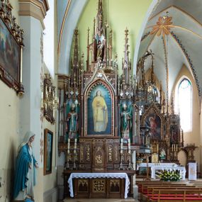 Zdjęcie nr 1: Neogotycki, przyścienny, jednokondygnacyjny ołtarz Matki Boskiej Różańcowej uzyskał architektoniczną strukturę ze zwieńczeniem. Kolorystyka ołtarza utrzymana została w tonacji ciemnego, bejcowanego drewna. Detale, ornamenty zostały wyzłocone, natomiast wypełnienia maswerków i ram wimperg są białe. Z kolei pole ramy głównego obrazu wykonano jako czerwone. Retabulum ustawiono na podwójnych gradusach zaokrąglonych od przodu. Stipes ołtarzowy uzyskał kształt prostopadłościanu z trzema czworobocznymi płycinami od frontu, ujętymi złoconymi i profilowanymi obramieniami. Płyciny rozdzielają  półkolumienki na wysokich cokolikach. Dwie skrajne płyciny stipesu wypełniono u góry maswerkiem, natomiast w środkowej znalazł się równoramienny krzyż wpisany w czteroliść. Stipes podtrzymuje drewnianą mensę z portatylem. Ołtarz przylega do wysokiego, prostopadłościennego cokołu flankowanego po bokach kolumienkami, na którym wspiera się cała nastawa. Widoczne jego partie zdobią prostokątne płyciny w obramieniach. Na cokole wspiera się predella podzielona płytkimi, prostokątnymi płycinami zakończonymi ostrołukowymi arkadkami z noskami, wypełnionymi płaskorzeźbionym i złoconym ornamentem roślinnym. Pośrodku, w przerwie między płycinami predelli, usytuowano prostopadłościenne tabernakulum w formie kapliczki, zwieńczone łukiem siodłowym, flankowane dwoma pinaklami. Ostrołukowe drzwiczki tabernakulum zdobi skrzyżowana z krzyżem kotwica oraz wyobrażenie Boskiego Serca Pana Jezusa. Poniżej widoczna jest girlanda różana. Predella wspiera trójosiową kondygnację ze zwieńczeniem. Na osi środkowej usytuowano płytką, prostokątną wnękę zakończoną ostrołukiem z arkaturą. Flankują ją smukłe kolumienki na wysokich cokolikach wspierające wysokie pinakle. Ponad wnęką widoczna jest wimperga z maswerkiem dekorowana czołgankami i kwiatonem. We wnęce umieszczono płaskorzeźbione i polichromowane przedstawienie Matki Boskiej Różańcowej ze św. Dominikiem i św. Katarzyną ze Sieny, a na zasuwie obraz ze św. Barbarą. W osiach skrajnych, pod gotyckimi baldachimami z wimpergami, rozdzielonymi pinaklami, ustawiono w niszach na postumentach figury św. Wojciecha i św. Stanisława. Święci zostali podpisani na postumentach. Konchy nisz są jasnoniebieskie natomiast ich ścianki zielone. Boki baldachimów udekorowano małymi wimpergami rozdzielonymi smukłymi pinaklami z kwiatonami i czołgankami. Baldachimy przechodzą w smukłe, ażurowe fiale dekorowane pinaklami i czołgankami oraz kwiatonami. Zwieńczenie nastawy na osi środkowej uzyskało kształt otwartej kapliczki z niszą zakończoną smukłą fialą z iglicą, dekorowaną czołgankami i kwiatonem. Po bokach kapliczki znajdują się ażurowe przypory wypełnione maswerkiem, flankowane pinaklami. W niszy umieszczono figurę św. Józefa z Dzieciątkiem. Całość retabulum flankują uszaki w formie ażurowych przypór, wypełnionych maswerkami i zdobionych parą pinakli.

