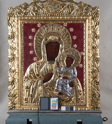 Zdjęcie nr 2: Feretron w typie obrazowym osadzony na niewysokiej podstawie z parą otworów na drążki. Pola obrazowe w kształcie stojących prostokątów ujmuje dekoracyjna rama z rzeźbionym motywem wici winnej latorośli, zwieńczona medalionem z monogramem chrystologicznym na awersie i maryjnym na rewersie. Awers feretronu zajmuje półpostaciowy wizerunek Jezusa w typie Ecce Homo. Jezus zwrócony jest nieznacznie w trzech czwartych w prawo. Przechyloną głowę charakteryzuje pociągła twarz o delikatnych rysach, długim nosie i krótkim, brązowym zaroście. Długie, falowane włosy opadają na barki. Głowę wieńczy cierniowa korona i okala promienisty nimb. Na czole i barkach widoczne są drobne stróżki krwi. Nagi tors Jezusa charakteryzuje rytmiczny układ żeber. Skrzyżowane na wysokości talii, zgięte w łokciach ręce związane są w nadgarstkach sznurem, w lewej dłoni trzyma pojedynczą trzcinę. Na ramiona Jezusa narzucony jest osłaniający biodra, zdobiony motywem kwiatowym płaszcz. Elementy takie jak nimb, korona cierniowa, sznur, trzcina i płaszcz są płaskorzeźbione, złocone i srebrzone. Tło utrzymane jest w odcieniu szafirowym. 
Rewers feretronu stanowi wizerunek Matki Boskiej Częstochowskiej. Ukazana półpostaciowo, zwrócona frontalnie Maria ma nieznacznie w trzech czwartych w lewo skierowaną głowę. Pociągłą, owalną twarz charakteryzują linearnie opracowane rysy o nieco przymkniętych oczach, długim prostym nosie i niewielkich ustach. Maria ubrana jest w suknię i osłaniający jej głowę i sylwetkę płaszcz. Prawą, uniesioną na wysokości klatki piersiowej dłonią o wyprostowanych palcach wskazuje na siedzące na jej lewej ręce Dzieciątko zwrócone w trzech czwartych w prawo. Okrągłą twarz Jezusa charakteryzują rysy dorosłego człowieka, o podobnym do Marii typie fizjonomii. Ubrany jest w długą suknię o trójkątnym dekolcie. Prawą rękę unosi w geście błogosławieństwa, lewą ujmuje trzymaną na kolanach zamkniętą księgę. Karnacje postaci są ciemne, a ich głowy wieńczą korony w typie otwartym i okalają nimby z motywem promieni oraz wieniec 12 gwiazd. Szaty, korony, nimby, gwiazdy i księga są płaskorzeźbione, złocone i srebrzone. Tło utrzymane jest w odcieniu czerwieni.        
