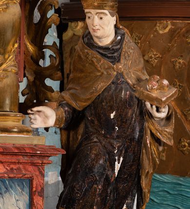 Zdjęcie nr 10: Nastawa ołtarzowa otrzymała formę jednokondygnacyjnej i jednoosiowej struktury architektonicznej wspartej na dwóch złoconych i kręconych kolumnach ze zwieńczeniem. Całość struktury pokryta jest marmoryzacją w kolorze palonej sieny. Drewniana mensa z portatylem o ściętych narożach wspiera się na prostopadłościennym stipesie ołtarzowym z fazowanym cokolikiem, ustawionym na stopniu. W miejscu ściętych naroży stipesu wprowadzono od frontu dwa srebrzone i złocone spływy wolutowe dodatkowo dekorowane motywem kampanuli. Przód stipesu zdobi jasna marmoryzacja oraz dwie poziome, płaskorzeźbione i złocone listwy z motywem ornamentu rocaille&#039;owego umieszczone pod mensą i nad cokolikiem. W centrum retabulum znalazł się obraz Matki Boskiej z Dzieciątkiem w typie Piekarskim zdobiony drewnianą, złoconą sukienką wotywną. Ponad obrazem w profilowanych, złotych ramach umieszczono płaskorzeźbiony i złocony ornament z motywem suchego liścia akantowego, zamknięty fantazyjnym obramieniem. Obraz flankują dwie złocone, spiralne kolumny z korynckimi kapitelami o trzonach zdobionych wicią roślinno-kwiatową. Na wysokich postumentach, których boki zdobią płyciny ujęte w profilowane listwy, ustawiono kolumny. Pomiędzy postumentami pierwotnie znajdowało się niezachowane dziś tabernakulum, flankowane zachowaną po bokach ażurową, złoconą wicią roślinną. Kolumny podtrzymują wysokie imposty zdobione ornamentem roślinnym, na których wsparto wyłamane na środku i mocno wysunięte do przodu belkowanie. W części środkowej silnie artykułowane, wyłamane belkowanie podniesiono do góry wieńcząc go rzeźbionym owalem imitującym wieniec laurowy, wypełnionym malowanym przedstawieniem gołębicy Ducha Świętego. Otacza go ażurowa dekoracja utworzona ze złoconej, suchej wici akantowej oraz ustawiona na szczycie waza płomienista. Ponad belkowaniem na przedłużeniu kolumn, na wysokich cokołach, umieszczono figury aniołów z rozpostartymi skrzydłami, które w jednej ręce trzymają lance, a w drugiej kartusze herbowe. Anioł z lewej strony trzyma kartusz z godłem herbu Jastrzębiec, natomiast anioł z prawej kartusz z godłem herbu Kornicz. Po bokach kolumn ustawiono z lewej figurę św. Andrzeja Apostoła, a z prawej św. Mikołaja biskupa. Retabulum flankują dwa ażurowe, złocone uszaki utworzone ze stylizowanej suchej wici akantowej.