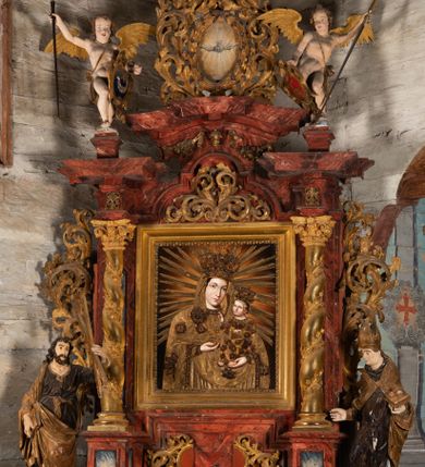 Zdjęcie nr 1: Nastawa ołtarzowa otrzymała formę jednokondygnacyjnej i jednoosiowej struktury architektonicznej wspartej na dwóch złoconych i kręconych kolumnach ze zwieńczeniem. Całość struktury pokryta jest marmoryzacją w kolorze palonej sieny. Drewniana mensa z portatylem o ściętych narożach wspiera się na prostopadłościennym stipesie ołtarzowym z fazowanym cokolikiem, ustawionym na stopniu. W miejscu ściętych naroży stipesu wprowadzono od frontu dwa srebrzone i złocone spływy wolutowe dodatkowo dekorowane motywem kampanuli. Przód stipesu zdobi jasna marmoryzacja oraz dwie poziome, płaskorzeźbione i złocone listwy z motywem ornamentu rocaille&#039;owego umieszczone pod mensą i nad cokolikiem. W centrum retabulum znalazł się obraz Matki Boskiej z Dzieciątkiem w typie Piekarskim zdobiony drewnianą, złoconą sukienką wotywną. Ponad obrazem w profilowanych, złotych ramach umieszczono płaskorzeźbiony i złocony ornament z motywem suchego liścia akantowego, zamknięty fantazyjnym obramieniem. Obraz flankują dwie złocone, spiralne kolumny z korynckimi kapitelami o trzonach zdobionych wicią roślinno-kwiatową. Na wysokich postumentach, których boki zdobią płyciny ujęte w profilowane listwy, ustawiono kolumny. Pomiędzy postumentami pierwotnie znajdowało się niezachowane dziś tabernakulum, flankowane zachowaną po bokach ażurową, złoconą wicią roślinną. Kolumny podtrzymują wysokie imposty zdobione ornamentem roślinnym, na których wsparto wyłamane na środku i mocno wysunięte do przodu belkowanie. W części środkowej silnie artykułowane, wyłamane belkowanie podniesiono do góry wieńcząc go rzeźbionym owalem imitującym wieniec laurowy, wypełnionym malowanym przedstawieniem gołębicy Ducha Świętego. Otacza go ażurowa dekoracja utworzona ze złoconej, suchej wici akantowej oraz ustawiona na szczycie waza płomienista. Ponad belkowaniem na przedłużeniu kolumn, na wysokich cokołach, umieszczono figury aniołów z rozpostartymi skrzydłami, które w jednej ręce trzymają lance, a w drugiej kartusze herbowe. Anioł z lewej strony trzyma kartusz z godłem herbu Jastrzębiec, natomiast anioł z prawej kartusz z godłem herbu Kornicz. Po bokach kolumn ustawiono z lewej figurę św. Andrzeja Apostoła, a z prawej św. Mikołaja biskupa. Retabulum flankują dwa ażurowe, złocone uszaki utworzone ze stylizowanej suchej wici akantowej.