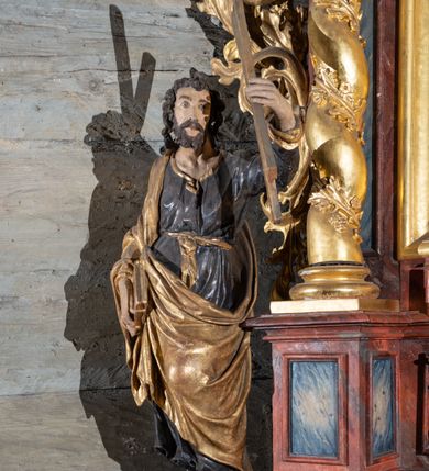 Zdjęcie nr 5: Nastawa ołtarzowa otrzymała formę jednokondygnacyjnej i jednoosiowej struktury architektonicznej wspartej na dwóch złoconych i kręconych kolumnach ze zwieńczeniem. Całość struktury pokryta jest marmoryzacją w kolorze palonej sieny. Drewniana mensa z portatylem o ściętych narożach wspiera się na prostopadłościennym stipesie ołtarzowym z fazowanym cokolikiem, ustawionym na stopniu. W miejscu ściętych naroży stipesu wprowadzono od frontu dwa srebrzone i złocone spływy wolutowe dodatkowo dekorowane motywem kampanuli. Przód stipesu zdobi jasna marmoryzacja oraz dwie poziome, płaskorzeźbione i złocone listwy z motywem ornamentu rocaille'owego umieszczone pod mensą i nad cokolikiem. W centrum retabulum znalazł się obraz Matki Boskiej z Dzieciątkiem w typie Piekarskim zdobiony drewnianą, złoconą sukienką wotywną. Ponad obrazem w profilowanych, złotych ramach umieszczono płaskorzeźbiony i złocony ornament z motywem suchego liścia akantowego, zamknięty fantazyjnym obramieniem. Obraz flankują dwie złocone, spiralne kolumny z korynckimi kapitelami o trzonach zdobionych wicią roślinno-kwiatową. Na wysokich postumentach, których boki zdobią płyciny ujęte w profilowane listwy, ustawiono kolumny. Pomiędzy postumentami pierwotnie znajdowało się niezachowane dziś tabernakulum, flankowane zachowaną po bokach ażurową, złoconą wicią roślinną. Kolumny podtrzymują wysokie imposty zdobione ornamentem roślinnym, na których wsparto wyłamane na środku i mocno wysunięte do przodu belkowanie. W części środkowej silnie artykułowane, wyłamane belkowanie podniesiono do góry wieńcząc go rzeźbionym owalem imitującym wieniec laurowy, wypełnionym malowanym przedstawieniem gołębicy Ducha Świętego. Otacza go ażurowa dekoracja utworzona ze złoconej, suchej wici akantowej oraz ustawiona na szczycie waza płomienista. Ponad belkowaniem na przedłużeniu kolumn, na wysokich cokołach, umieszczono figury aniołów z rozpostartymi skrzydłami, które w jednej ręce trzymają lance, a w drugiej kartusze herbowe. Anioł z lewej strony trzyma kartusz z godłem herbu Jastrzębiec, natomiast anioł z prawej kartusz z godłem herbu Kornicz. Po bokach kolumn ustawiono z lewej figurę św. Andrzeja Apostoła, a z prawej św. Mikołaja biskupa. Retabulum flankują dwa ażurowe, złocone uszaki utworzone ze stylizowanej suchej wici akantowej.