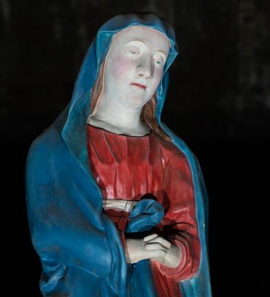 Zdjęcie nr 1: Figura ukazuje w całej postaci stojącą na płaskim postumencie w nieznacznym kontrapoście Matkę Boską. Maria została przedstawiona frontalnie z nieznacznie pochyloną głową w lewą stronę oraz boleśnie zaplecionymi dłońmi trzymanymi na wysokości pasa. Ma pociągłą twarz o jasnej karnacji, duży nos, wąskie usta i półprzymknięte oczy. Ubrana jest w niebieski maforion, spod którego widać brązowe włosy spływające na ramiona oraz czerwoną suknię przewiązaną w talii białą szarfą. Prawa poła maforionu podwinięta jest pod prawą rękę. Spod sukni widoczne są jej bose stopy.