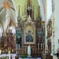 Zdjęcie nr 1: Neogotycki, przyścienny, jednokondygnacyjny ołtarz Świętej Rodziny uzyskał architektoniczną strukturę ze zwieńczeniem. Kolorystyka ołtarza utrzymana została w tonacji ciemnego, bejcowanego drewna. Detale, ornamenty zostały wyzłocone, natomiast wypełnienia maswerków i ram wimperg są białe. Z kolei pole ramy głównego obrazu wykonano jako czerwone. Retabulum ustawiono na podwójnych gradusach zaokrąglonych od przodu. Stipes ołtarzowy uzyskał kształt prostopadłościanu z trzema czworobocznymi płycinami od frontu, ujętymi złoconymi i profilowanymi obramieniami. Płyciny rozdzielają półkolumienki na wysokich cokolikach. Dwie skrajne płyciny stipesu wypełniono u góry maswerkiem, natomiast w środkowej znalazł się równoramienny krzyż wpisany w czteroliść. Stipes podtrzymuje drewnianą mensę z portatylem. Ołtarz przylega do wysokiego, prostopadłościennego cokołu flankowanego po bokach kolumienkami, na którym wspiera się cała nastawa. Widoczne jego partie zdobią prostokątne płyciny w obramieniach. Na cokole wspiera się predella podzielona płytkimi, prostokątnymi płycinami zakończonymi ostrołukowymi arkadkami z noskami, wypełnionymi płaskorzeźbionym i złoconym ornamentem roślinnym. Pośrodku, w przerwie między płycinami predelli, usytuowano prostopadłościenne tabernakulum w formie kapliczki, zwieńczone łukiem siodłowym, flankowane dwoma pinaklami. Ostrołukowe drzwiczki tabernakulum zdobi skrzyżowana z krzyżem kotwica oraz wyobrażenie Boskiego Serca Pana Jezusa. Poniżej widoczna jest girlanda różana. Nad drzwiczkami umieszczono stylizowany ornament roślinny. Predella wspiera trójosiową kondygnację ze zwieńczeniem. Na osi środkowej usytuowano płytką, prostokątną wnękę zakończoną ostrołukiem z arkaturą. Flankują ją smukłe kolumienki na wysokich cokolikach wspierające wysokie pinakle. Ponad wnęką widoczna jest wimperga z maswerkiem dekorowana czołgankami i kwiatonem. We wnęce umieszczono pełnoplastyczne rzeźby Matki Boskiej i św. Józefa, pomiędzy którymi stoi mały Jezus, a na zasuwie obraz Matki Boskiej Nieustającej Pomocy. W osiach skrajnych, pod gotyckimi baldachimami z wimpergami, rozdzielonymi pinaklami, ustawiono w niszach na postumentach figury św. Jana Kantego i św. Kazimierza Królewicza. Święci są podpisani na postumentach. Konchy nisz są jasnoniebieskie natomiast ich ścianki zielone. Boki baldachimów udekorowano małymi wimpergami rozdzielonymi smukłymi pinaklami z kwiatonami i czołgankami. Baldachimy przechodzą w smukłe, ażurowe fiale dekorowane pinaklami i czołgankami oraz kwiatonami. Zwieńczenie nastawy na osi środkowej uzyskało kształt otwartej kapliczki z niszą zakończoną smukłą fialą z iglicą, dekorowaną czołgankami i kwiatonem. Po bokach kapliczki znajdują się przypory dekorowane maswerkiem i flankowane pinaklami. W niszy umieszczono figurę św. Antoniego z Padwy, którego podpisano na postumencie. Całość retabulum flankują uszaki w formie ażurowych przypór, wypełnionych maswerkami i zdobionych parą pinakli.
