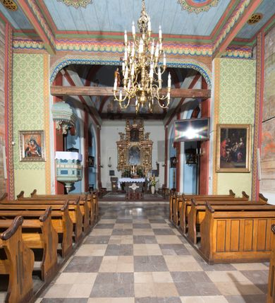 Zdjęcie nr 5: Kościół, otoczony starodrzewiem, położony jest na niewielkim wzniesieniu ponad stawami w centrum wsi. Jest to budowla drewniano-murowana, orientowana. Nawa została wzniesiona w 1518 roku na zrąb na rzucie zbliżonym do kwadratu, nakryta płaskim stropem. Od zachodu do nawy przylega wzniesiona w tym samym roku wieża o konstrukcji słupowej, pierwotnie kwadratowa o pochyłych ścianach, w 1782 roku poszerzona przez obudowanie drugą konstrukcją, prawie pionową. Wieża, w całości szalowana, poprzedzona niewielką kruchtą, w połowie wysokości jest opasana daszkiem pulpitowym. Jej hełm posiada kształt kopuły zwieńczonej ostrosłupem. Od południa do nawy przylega drewniana kruchta z 1924 roku, a od wschodu murowane prezbiterium z 1931 roku. Prezbiterium otwiera się podwójnymi arkadami na dwie kaplice boczne - wzniesioną od południa w 1861 roku z kryptą grobową Duninów oraz kaplicę przylegającą od północy zbudowaną w 1931 roku. Jego przestrzeń nakryto sklepieniem kolebkowym na gurtach, zaś dwuprzęsłowe kaplice sklepieniem krzyżowym. Za prezbiterium wznosi się murowana, piętrowa zakrystia z XVII wieku przykryta sklepieniem nieckowym z lunetami i małym zwierciadłem, zdobionym monogramem maryjnym. Jednokalenicowy dach nawy i prezbiterium pokryty jest dachówką. Nad końcu dachu nawy od wschodu nadwieszono wieżyczkę na sygnaturkę z latarnią i cebulastą banią, zwieńczoną krzyżem. Zakrystia nakryta została namiotowym dachem polskim, także pokrytym dachówką. Na zewnętrznych ścianach części murowanej umieszczono kilka epitafiów przeniesionych z wnętrza kościoła. Wewnątrz prezbiterium na ścianie wschodniej, nad wejściem do zakrystii, zawieszono manierystyczny, dwukondygnacyjny ołtarz główny z XVII wieku z uszakami zdobionymi herbami Starykoń i Jelita. Przy ścianie północnej, w miejscu połączenia nawy drewnianej z murowanym prezbiterium, usytuowano w 1931 roku ambonę oraz kamienną chrzcielnicę z 1658 roku. Belkę tęczową zdobi osiemnastowieczna grupa Ukrzyżowania. W kaplicach bocznych ustawiono dwa neobarokowe ołtarze boczne.  