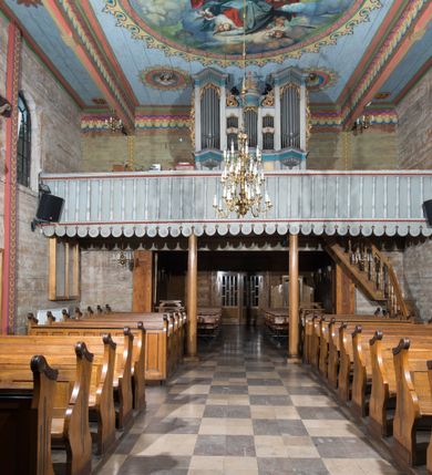 Zdjęcie nr 12: Kościół, otoczony starodrzewiem, położony jest na niewielkim wzniesieniu ponad stawami w centrum wsi. Jest to budowla drewniano-murowana, orientowana. Nawa została wzniesiona w 1518 roku na zrąb na rzucie zbliżonym do kwadratu, nakryta płaskim stropem. Od zachodu do nawy przylega wzniesiona w tym samym roku wieża o konstrukcji słupowej, pierwotnie kwadratowa o pochyłych ścianach, w 1782 roku poszerzona przez obudowanie drugą konstrukcją, prawie pionową. Wieża, w całości szalowana, poprzedzona niewielką kruchtą, w połowie wysokości jest opasana daszkiem pulpitowym. Jej hełm posiada kształt kopuły zwieńczonej ostrosłupem. Od południa do nawy przylega drewniana kruchta z 1924 roku, a od wschodu murowane prezbiterium z 1931 roku. Prezbiterium otwiera się podwójnymi arkadami na dwie kaplice boczne - wzniesioną od południa w 1861 roku z kryptą grobową Duninów oraz kaplicę przylegającą od północy zbudowaną w 1931 roku. Jego przestrzeń nakryto sklepieniem kolebkowym na gurtach, zaś dwuprzęsłowe kaplice sklepieniem krzyżowym. Za prezbiterium wznosi się murowana, piętrowa zakrystia z XVII wieku przykryta sklepieniem nieckowym z lunetami i małym zwierciadłem, zdobionym monogramem maryjnym. Jednokalenicowy dach nawy i prezbiterium pokryty jest dachówką. Nad końcu dachu nawy od wschodu nadwieszono wieżyczkę na sygnaturkę z latarnią i cebulastą banią, zwieńczoną krzyżem. Zakrystia nakryta została namiotowym dachem polskim, także pokrytym dachówką. Na zewnętrznych ścianach części murowanej umieszczono kilka epitafiów przeniesionych z wnętrza kościoła. Wewnątrz prezbiterium na ścianie wschodniej, nad wejściem do zakrystii, zawieszono manierystyczny, dwukondygnacyjny ołtarz główny z XVII wieku z uszakami zdobionymi herbami Starykoń i Jelita. Przy ścianie północnej, w miejscu połączenia nawy drewnianej z murowanym prezbiterium, usytuowano w 1931 roku ambonę oraz kamienną chrzcielnicę z 1658 roku. Belkę tęczową zdobi osiemnastowieczna grupa Ukrzyżowania. W kaplicach bocznych ustawiono dwa neobarokowe ołtarze boczne.  