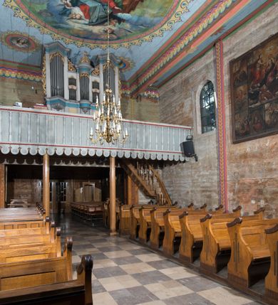 Zdjęcie nr 15: Kościół, otoczony starodrzewiem, położony jest na niewielkim wzniesieniu ponad stawami w centrum wsi. Jest to budowla drewniano-murowana, orientowana. Nawa została wzniesiona w 1518 roku na zrąb na rzucie zbliżonym do kwadratu, nakryta płaskim stropem. Od zachodu do nawy przylega wzniesiona w tym samym roku wieża o konstrukcji słupowej, pierwotnie kwadratowa o pochyłych ścianach, w 1782 roku poszerzona przez obudowanie drugą konstrukcją, prawie pionową. Wieża, w całości szalowana, poprzedzona niewielką kruchtą, w połowie wysokości jest opasana daszkiem pulpitowym. Jej hełm posiada kształt kopuły zwieńczonej ostrosłupem. Od południa do nawy przylega drewniana kruchta z 1924 roku, a od wschodu murowane prezbiterium z 1931 roku. Prezbiterium otwiera się podwójnymi arkadami na dwie kaplice boczne - wzniesioną od południa w 1861 roku z kryptą grobową Duninów oraz kaplicę przylegającą od północy zbudowaną w 1931 roku. Jego przestrzeń nakryto sklepieniem kolebkowym na gurtach, zaś dwuprzęsłowe kaplice sklepieniem krzyżowym. Za prezbiterium wznosi się murowana, piętrowa zakrystia z XVII wieku przykryta sklepieniem nieckowym z lunetami i małym zwierciadłem, zdobionym monogramem maryjnym. Jednokalenicowy dach nawy i prezbiterium pokryty jest dachówką. Nad końcu dachu nawy od wschodu nadwieszono wieżyczkę na sygnaturkę z latarnią i cebulastą banią, zwieńczoną krzyżem. Zakrystia nakryta została namiotowym dachem polskim, także pokrytym dachówką. Na zewnętrznych ścianach części murowanej umieszczono kilka epitafiów przeniesionych z wnętrza kościoła. Wewnątrz prezbiterium na ścianie wschodniej, nad wejściem do zakrystii, zawieszono manierystyczny, dwukondygnacyjny ołtarz główny z XVII wieku z uszakami zdobionymi herbami Starykoń i Jelita. Przy ścianie północnej, w miejscu połączenia nawy drewnianej z murowanym prezbiterium, usytuowano w 1931 roku ambonę oraz kamienną chrzcielnicę z 1658 roku. Belkę tęczową zdobi osiemnastowieczna grupa Ukrzyżowania. W kaplicach bocznych ustawiono dwa neobarokowe ołtarze boczne.  