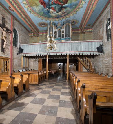 Zdjęcie nr 14: Kościół, otoczony starodrzewiem, położony jest na niewielkim wzniesieniu ponad stawami w centrum wsi. Jest to budowla drewniano-murowana, orientowana. Nawa została wzniesiona w 1518 roku na zrąb na rzucie zbliżonym do kwadratu, nakryta płaskim stropem. Od zachodu do nawy przylega wzniesiona w tym samym roku wieża o konstrukcji słupowej, pierwotnie kwadratowa o pochyłych ścianach, w 1782 roku poszerzona przez obudowanie drugą konstrukcją, prawie pionową. Wieża, w całości szalowana, poprzedzona niewielką kruchtą, w połowie wysokości jest opasana daszkiem pulpitowym. Jej hełm posiada kształt kopuły zwieńczonej ostrosłupem. Od południa do nawy przylega drewniana kruchta z 1924 roku, a od wschodu murowane prezbiterium z 1931 roku. Prezbiterium otwiera się podwójnymi arkadami na dwie kaplice boczne - wzniesioną od południa w 1861 roku z kryptą grobową Duninów oraz kaplicę przylegającą od północy zbudowaną w 1931 roku. Jego przestrzeń nakryto sklepieniem kolebkowym na gurtach, zaś dwuprzęsłowe kaplice sklepieniem krzyżowym. Za prezbiterium wznosi się murowana, piętrowa zakrystia z XVII wieku przykryta sklepieniem nieckowym z lunetami i małym zwierciadłem, zdobionym monogramem maryjnym. Jednokalenicowy dach nawy i prezbiterium pokryty jest dachówką. Nad końcu dachu nawy od wschodu nadwieszono wieżyczkę na sygnaturkę z latarnią i cebulastą banią, zwieńczoną krzyżem. Zakrystia nakryta została namiotowym dachem polskim, także pokrytym dachówką. Na zewnętrznych ścianach części murowanej umieszczono kilka epitafiów przeniesionych z wnętrza kościoła. Wewnątrz prezbiterium na ścianie wschodniej, nad wejściem do zakrystii, zawieszono manierystyczny, dwukondygnacyjny ołtarz główny z XVII wieku z uszakami zdobionymi herbami Starykoń i Jelita. Przy ścianie północnej, w miejscu połączenia nawy drewnianej z murowanym prezbiterium, usytuowano w 1931 roku ambonę oraz kamienną chrzcielnicę z 1658 roku. Belkę tęczową zdobi osiemnastowieczna grupa Ukrzyżowania. W kaplicach bocznych ustawiono dwa neobarokowe ołtarze boczne.  