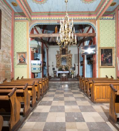 Zdjęcie nr 4: Kościół, otoczony starodrzewiem, położony jest na niewielkim wzniesieniu ponad stawami w centrum wsi. Jest to budowla drewniano-murowana, orientowana. Nawa została wzniesiona w 1518 roku na zrąb na rzucie zbliżonym do kwadratu, nakryta płaskim stropem. Od zachodu do nawy przylega wzniesiona w tym samym roku wieża o konstrukcji słupowej, pierwotnie kwadratowa o pochyłych ścianach, w 1782 roku poszerzona przez obudowanie drugą konstrukcją, prawie pionową. Wieża, w całości szalowana, poprzedzona niewielką kruchtą, w połowie wysokości jest opasana daszkiem pulpitowym. Jej hełm posiada kształt kopuły zwieńczonej ostrosłupem. Od południa do nawy przylega drewniana kruchta z 1924 roku, a od wschodu murowane prezbiterium z 1931 roku. Prezbiterium otwiera się podwójnymi arkadami na dwie kaplice boczne - wzniesioną od południa w 1861 roku z kryptą grobową Duninów oraz kaplicę przylegającą od północy zbudowaną w 1931 roku. Jego przestrzeń nakryto sklepieniem kolebkowym na gurtach, zaś dwuprzęsłowe kaplice sklepieniem krzyżowym. Za prezbiterium wznosi się murowana, piętrowa zakrystia z XVII wieku przykryta sklepieniem nieckowym z lunetami i małym zwierciadłem, zdobionym monogramem maryjnym. Jednokalenicowy dach nawy i prezbiterium pokryty jest dachówką. Nad końcu dachu nawy od wschodu nadwieszono wieżyczkę na sygnaturkę z latarnią i cebulastą banią, zwieńczoną krzyżem. Zakrystia nakryta została namiotowym dachem polskim, także pokrytym dachówką. Na zewnętrznych ścianach części murowanej umieszczono kilka epitafiów przeniesionych z wnętrza kościoła. Wewnątrz prezbiterium na ścianie wschodniej, nad wejściem do zakrystii, zawieszono manierystyczny, dwukondygnacyjny ołtarz główny z XVII wieku z uszakami zdobionymi herbami Starykoń i Jelita. Przy ścianie północnej, w miejscu połączenia nawy drewnianej z murowanym prezbiterium, usytuowano w 1931 roku ambonę oraz kamienną chrzcielnicę z 1658 roku. Belkę tęczową zdobi osiemnastowieczna grupa Ukrzyżowania. W kaplicach bocznych ustawiono dwa neobarokowe ołtarze boczne.  