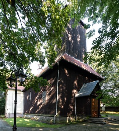 Zdjęcie nr 2: Kościół, otoczony starodrzewiem, położony jest na niewielkim wzniesieniu ponad stawami w centrum wsi. Jest to budowla drewniano-murowana, orientowana. Nawa została wzniesiona w 1518 roku na zrąb na rzucie zbliżonym do kwadratu, nakryta płaskim stropem. Od zachodu do nawy przylega wzniesiona w tym samym roku wieża o konstrukcji słupowej, pierwotnie kwadratowa o pochyłych ścianach, w 1782 roku poszerzona przez obudowanie drugą konstrukcją, prawie pionową. Wieża, w całości szalowana, poprzedzona niewielką kruchtą, w połowie wysokości jest opasana daszkiem pulpitowym. Jej hełm posiada kształt kopuły zwieńczonej ostrosłupem. Od południa do nawy przylega drewniana kruchta z 1924 roku, a od wschodu murowane prezbiterium z 1931 roku. Prezbiterium otwiera się podwójnymi arkadami na dwie kaplice boczne - wzniesioną od południa w 1861 roku z kryptą grobową Duninów oraz kaplicę przylegającą od północy zbudowaną w 1931 roku. Jego przestrzeń nakryto sklepieniem kolebkowym na gurtach, zaś dwuprzęsłowe kaplice sklepieniem krzyżowym. Za prezbiterium wznosi się murowana, piętrowa zakrystia z XVII wieku przykryta sklepieniem nieckowym z lunetami i małym zwierciadłem, zdobionym monogramem maryjnym. Jednokalenicowy dach nawy i prezbiterium pokryty jest dachówką. Nad końcu dachu nawy od wschodu nadwieszono wieżyczkę na sygnaturkę z latarnią i cebulastą banią, zwieńczoną krzyżem. Zakrystia nakryta została namiotowym dachem polskim, także pokrytym dachówką. Na zewnętrznych ścianach części murowanej umieszczono kilka epitafiów przeniesionych z wnętrza kościoła. Wewnątrz prezbiterium na ścianie wschodniej, nad wejściem do zakrystii, zawieszono manierystyczny, dwukondygnacyjny ołtarz główny z XVII wieku z uszakami zdobionymi herbami Starykoń i Jelita. Przy ścianie północnej, w miejscu połączenia nawy drewnianej z murowanym prezbiterium, usytuowano w 1931 roku ambonę oraz kamienną chrzcielnicę z 1658 roku. Belkę tęczową zdobi osiemnastowieczna grupa Ukrzyżowania. W kaplicach bocznych ustawiono dwa neobarokowe ołtarze boczne.  