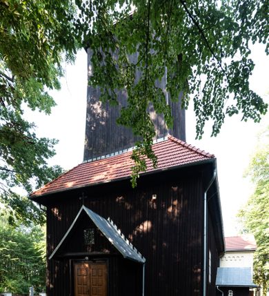 Zdjęcie nr 13: Kościół, otoczony starodrzewiem, położony jest na niewielkim wzniesieniu ponad stawami w centrum wsi. Jest to budowla drewniano-murowana, orientowana. Nawa została wzniesiona w 1518 roku na zrąb na rzucie zbliżonym do kwadratu, nakryta płaskim stropem. Od zachodu do nawy przylega wzniesiona w tym samym roku wieża o konstrukcji słupowej, pierwotnie kwadratowa o pochyłych ścianach, w 1782 roku poszerzona przez obudowanie drugą konstrukcją, prawie pionową. Wieża, w całości szalowana, poprzedzona niewielką kruchtą, w połowie wysokości jest opasana daszkiem pulpitowym. Jej hełm posiada kształt kopuły zwieńczonej ostrosłupem. Od południa do nawy przylega drewniana kruchta z 1924 roku, a od wschodu murowane prezbiterium z 1931 roku. Prezbiterium otwiera się podwójnymi arkadami na dwie kaplice boczne - wzniesioną od południa w 1861 roku z kryptą grobową Duninów oraz kaplicę przylegającą od północy zbudowaną w 1931 roku. Jego przestrzeń nakryto sklepieniem kolebkowym na gurtach, zaś dwuprzęsłowe kaplice sklepieniem krzyżowym. Za prezbiterium wznosi się murowana, piętrowa zakrystia z XVII wieku przykryta sklepieniem nieckowym z lunetami i małym zwierciadłem, zdobionym monogramem maryjnym. Jednokalenicowy dach nawy i prezbiterium pokryty jest dachówką. Nad końcu dachu nawy od wschodu nadwieszono wieżyczkę na sygnaturkę z latarnią i cebulastą banią, zwieńczoną krzyżem. Zakrystia nakryta została namiotowym dachem polskim, także pokrytym dachówką. Na zewnętrznych ścianach części murowanej umieszczono kilka epitafiów przeniesionych z wnętrza kościoła. Wewnątrz prezbiterium na ścianie wschodniej, nad wejściem do zakrystii, zawieszono manierystyczny, dwukondygnacyjny ołtarz główny z XVII wieku z uszakami zdobionymi herbami Starykoń i Jelita. Przy ścianie północnej, w miejscu połączenia nawy drewnianej z murowanym prezbiterium, usytuowano w 1931 roku ambonę oraz kamienną chrzcielnicę z 1658 roku. Belkę tęczową zdobi osiemnastowieczna grupa Ukrzyżowania. W kaplicach bocznych ustawiono dwa neobarokowe ołtarze boczne.  