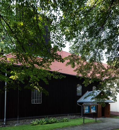 Zdjęcie nr 18: Kościół, otoczony starodrzewiem, położony jest na niewielkim wzniesieniu ponad stawami w centrum wsi. Jest to budowla drewniano-murowana, orientowana. Nawa została wzniesiona w 1518 roku na zrąb na rzucie zbliżonym do kwadratu, nakryta płaskim stropem. Od zachodu do nawy przylega wzniesiona w tym samym roku wieża o konstrukcji słupowej, pierwotnie kwadratowa o pochyłych ścianach, w 1782 roku poszerzona przez obudowanie drugą konstrukcją, prawie pionową. Wieża, w całości szalowana, poprzedzona niewielką kruchtą, w połowie wysokości jest opasana daszkiem pulpitowym. Jej hełm posiada kształt kopuły zwieńczonej ostrosłupem. Od południa do nawy przylega drewniana kruchta z 1924 roku, a od wschodu murowane prezbiterium z 1931 roku. Prezbiterium otwiera się podwójnymi arkadami na dwie kaplice boczne - wzniesioną od południa w 1861 roku z kryptą grobową Duninów oraz kaplicę przylegającą od północy zbudowaną w 1931 roku. Jego przestrzeń nakryto sklepieniem kolebkowym na gurtach, zaś dwuprzęsłowe kaplice sklepieniem krzyżowym. Za prezbiterium wznosi się murowana, piętrowa zakrystia z XVII wieku przykryta sklepieniem nieckowym z lunetami i małym zwierciadłem, zdobionym monogramem maryjnym. Jednokalenicowy dach nawy i prezbiterium pokryty jest dachówką. Nad końcu dachu nawy od wschodu nadwieszono wieżyczkę na sygnaturkę z latarnią i cebulastą banią, zwieńczoną krzyżem. Zakrystia nakryta została namiotowym dachem polskim, także pokrytym dachówką. Na zewnętrznych ścianach części murowanej umieszczono kilka epitafiów przeniesionych z wnętrza kościoła. Wewnątrz prezbiterium na ścianie wschodniej, nad wejściem do zakrystii, zawieszono manierystyczny, dwukondygnacyjny ołtarz główny z XVII wieku z uszakami zdobionymi herbami Starykoń i Jelita. Przy ścianie północnej, w miejscu połączenia nawy drewnianej z murowanym prezbiterium, usytuowano w 1931 roku ambonę oraz kamienną chrzcielnicę z 1658 roku. Belkę tęczową zdobi osiemnastowieczna grupa Ukrzyżowania. W kaplicach bocznych ustawiono dwa neobarokowe ołtarze boczne.  